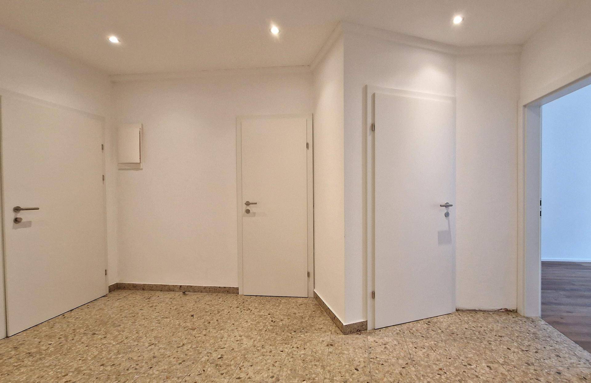 Heller Flur mit Terrazzoboden und mehreren weißen Türen, die zu verschiedenen Räumen führen.