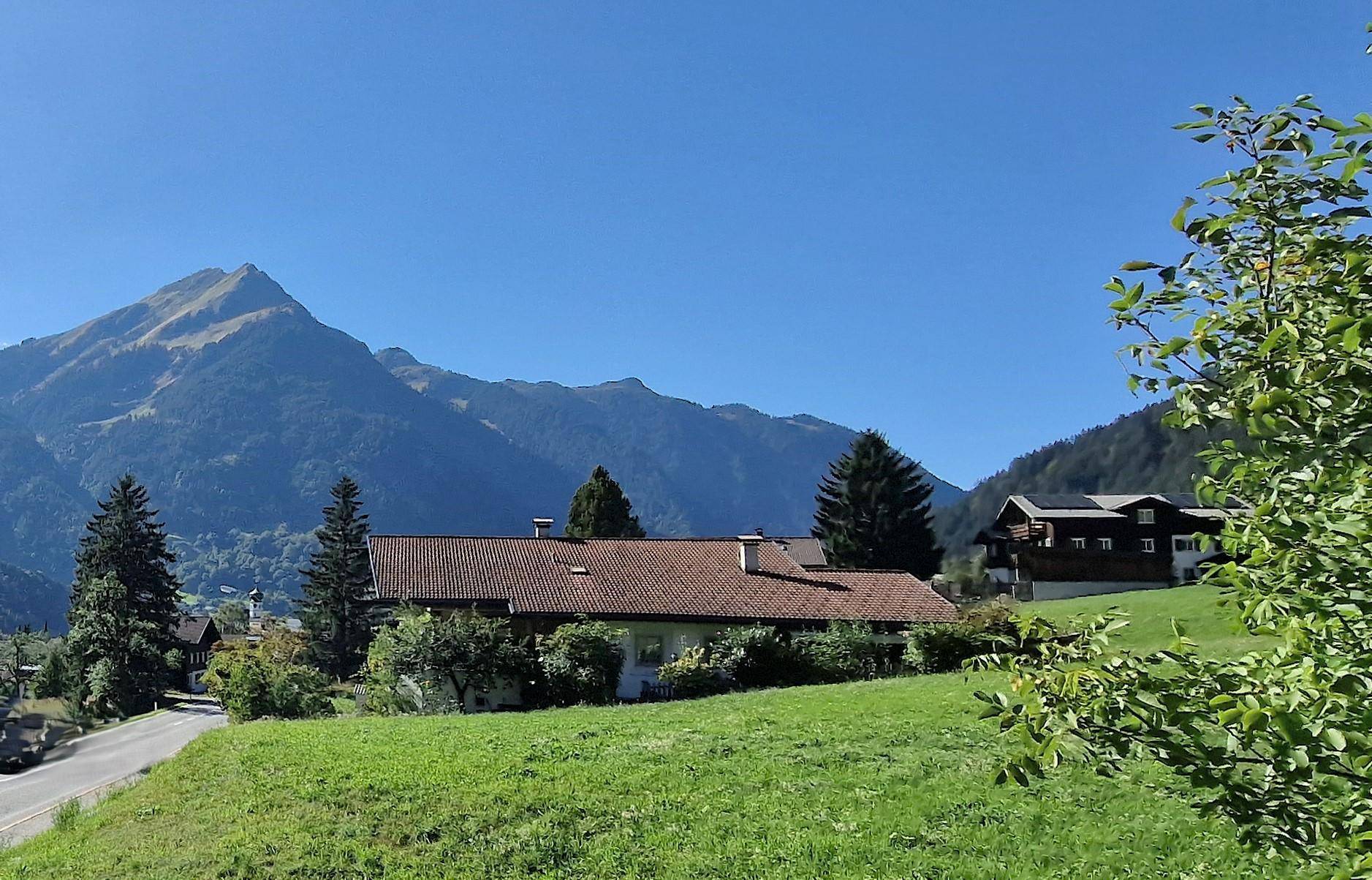 Idyllische Berglandschaft mit traditionellen Häusern, üppigen grünen Wiesen und klarem blauen Himmel.