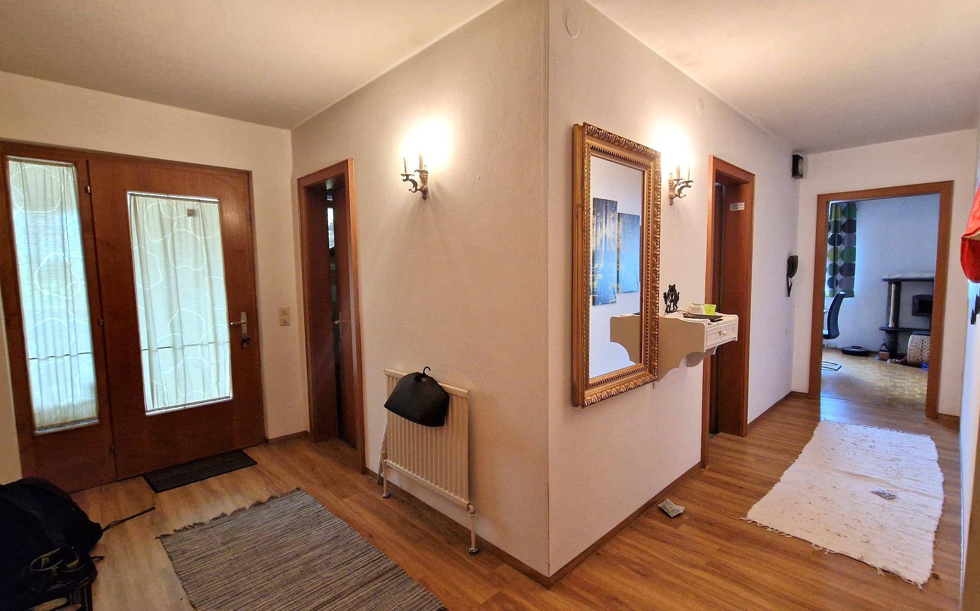 Heller Eingangsbereich mit Holzfußboden, dekorativem Spiegel und Zugang zu weiteren Räumen.