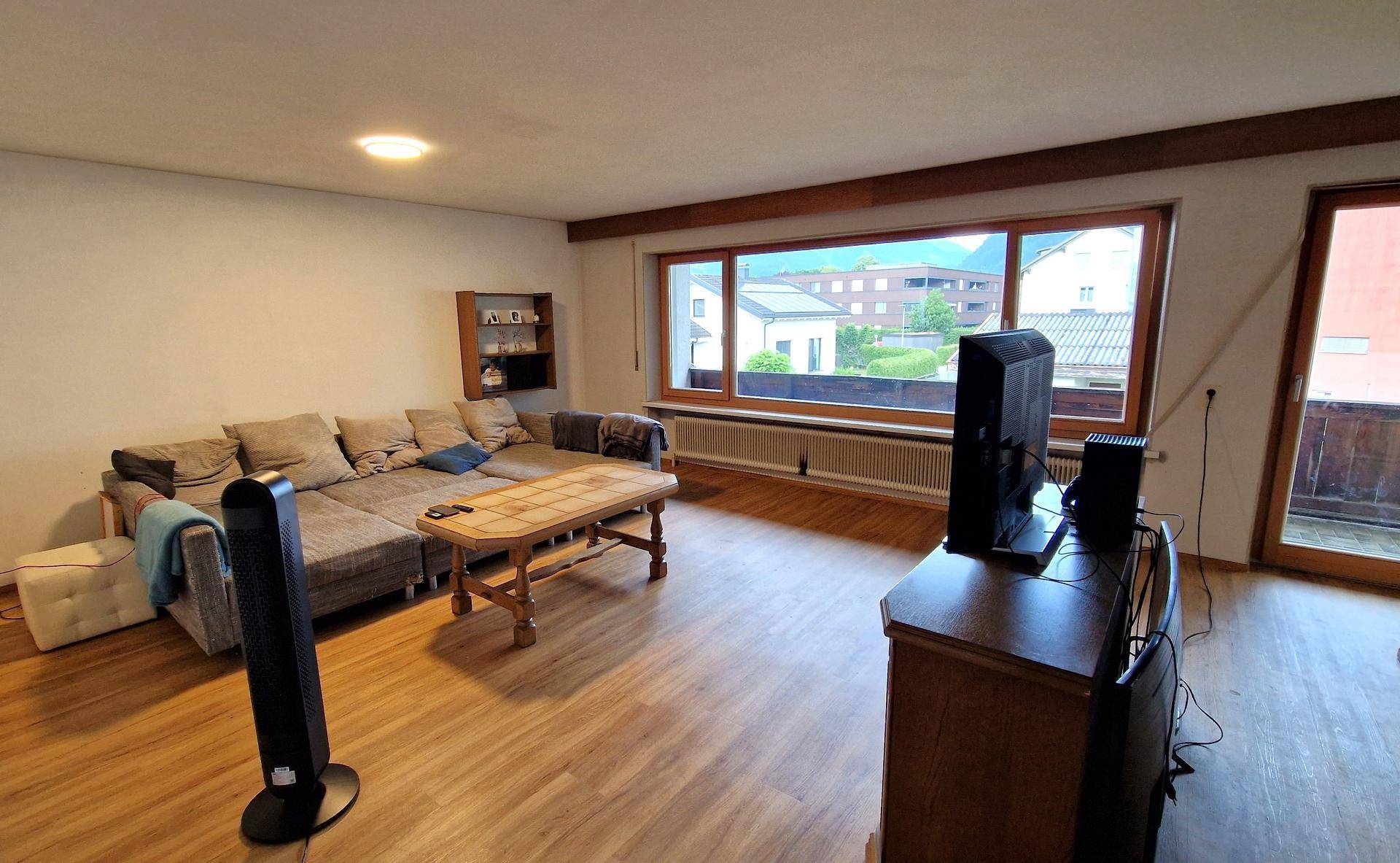 Helles Wohnzimmer mit Laminatboden, großem Fenster und Zugang zum Balkon.
