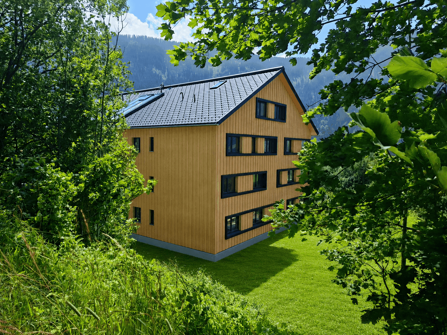 Das moderne Holzgebäude ist harmonisch in die grüne Berglandschaft eingebettet und von Bäumen umgeben.