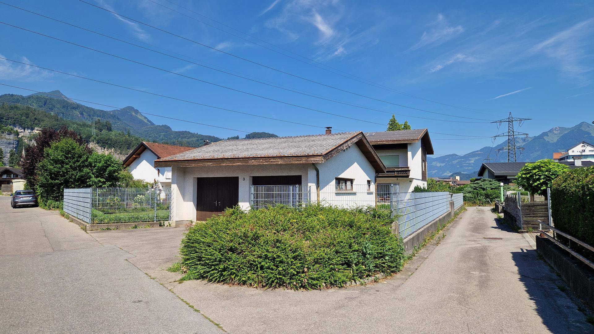 Zufahrt zum Haus mit Doppelgarage und gepflegter Bepflanzung in ländlicher Umgebung.