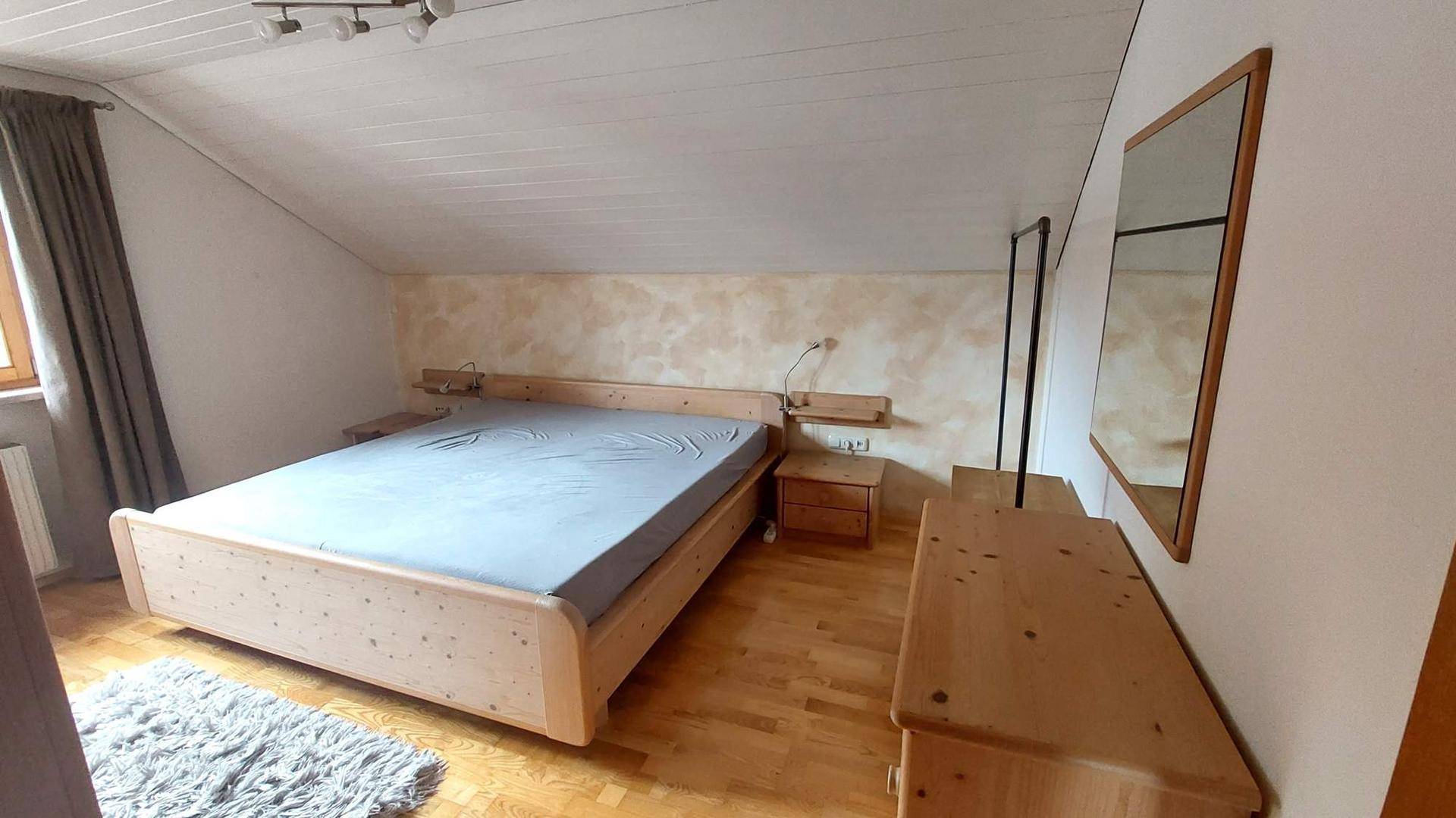 Gemütliches Schlafzimmer im Dachgeschoss mit Holzbett, hellem Holzboden und schräger Decke.