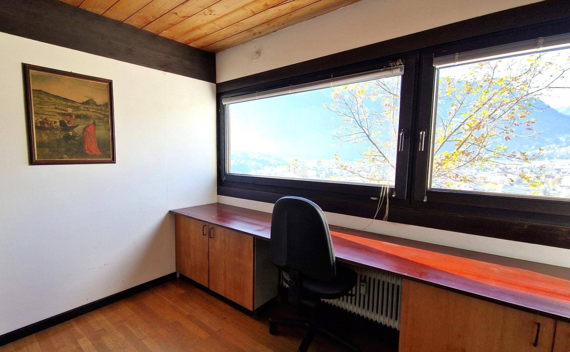 Arbeitsbereich mit Schreibtisch, Holzschränken und großem Fenster mit Ausblick.