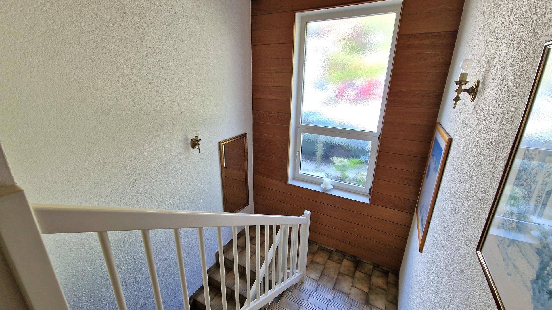 Treppenhaus mit Holzverkleidung und einem Fenster, das den Bereich mit Tageslicht versorgt.