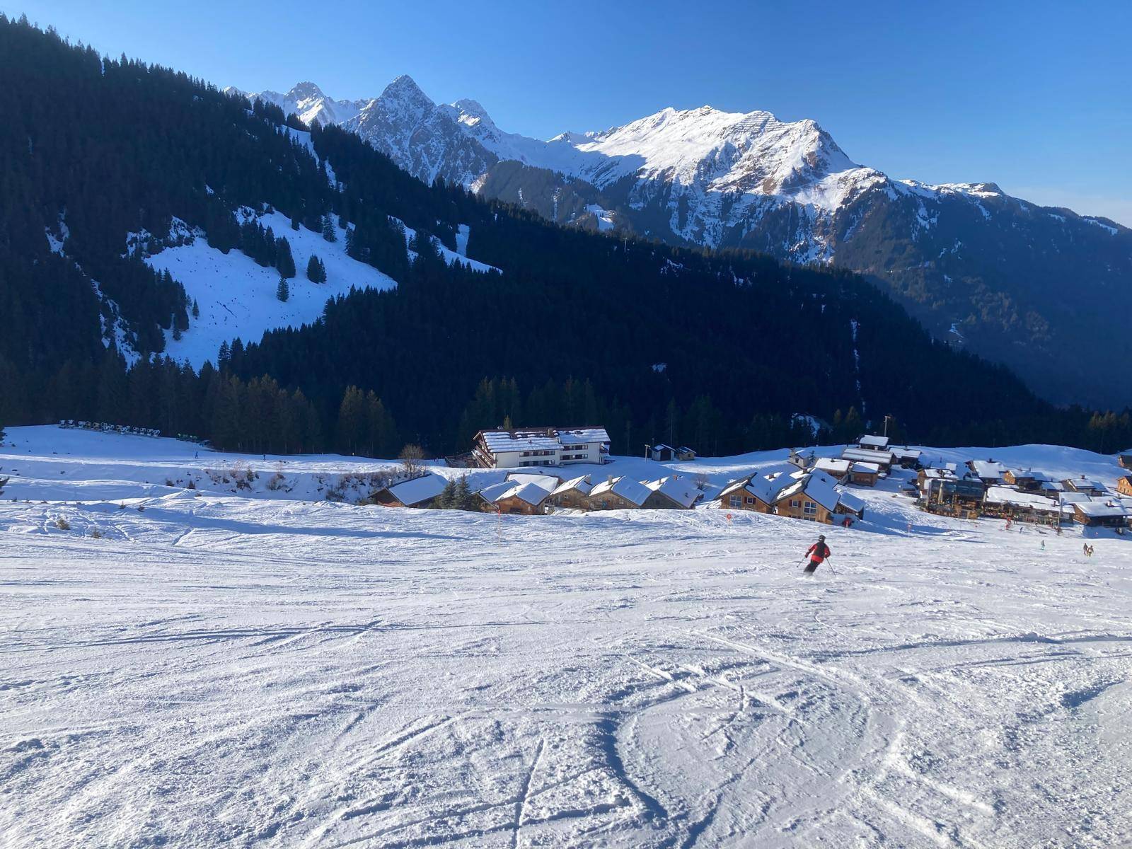 Weitläufige Schneelandschaft mit Skifahrern, Chalets und majestätischen Berggipfeln.