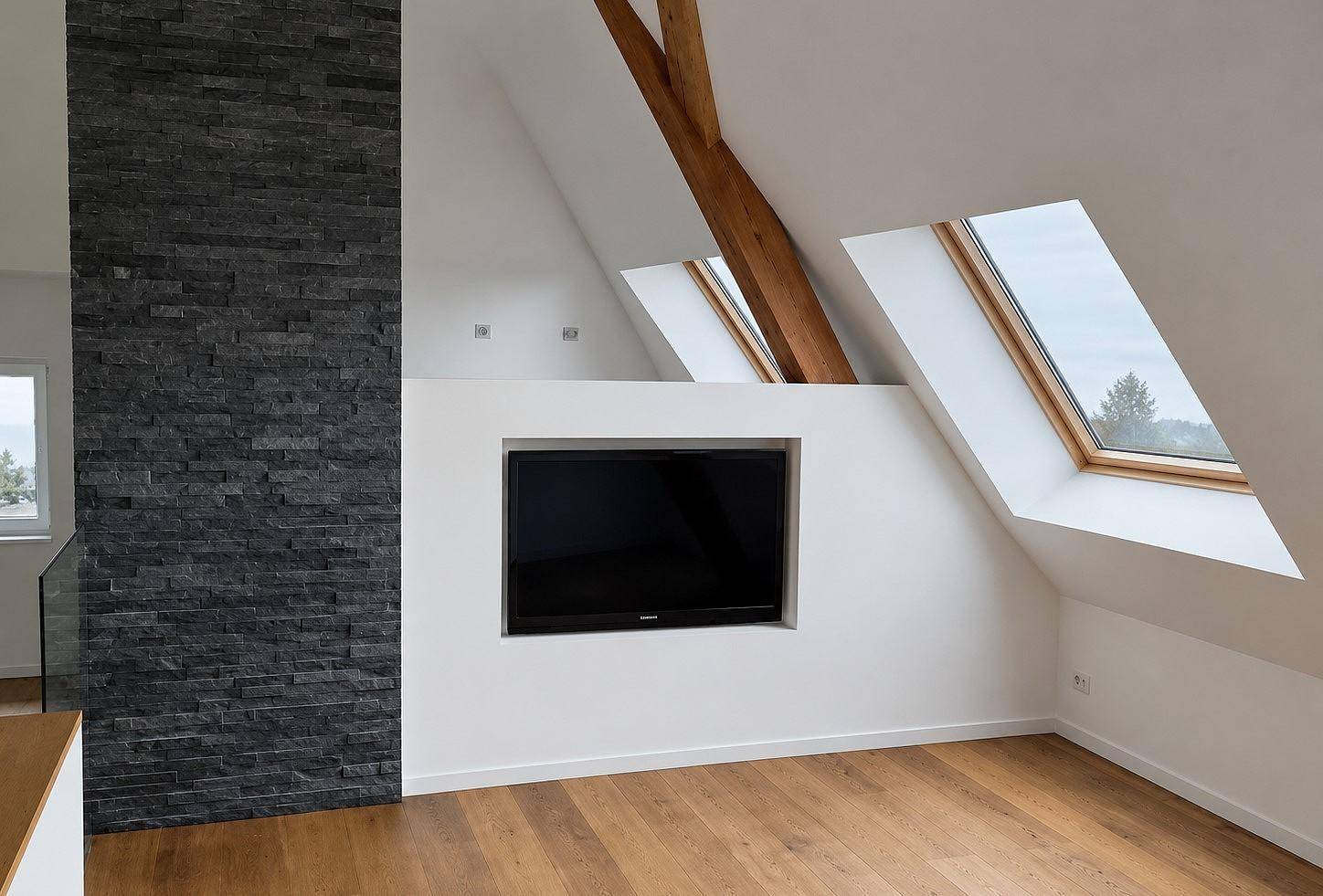 Heller Wohnbereich im Dachgeschoss mit Holzbalken, Dachfenstern und integriertem Fernseher.