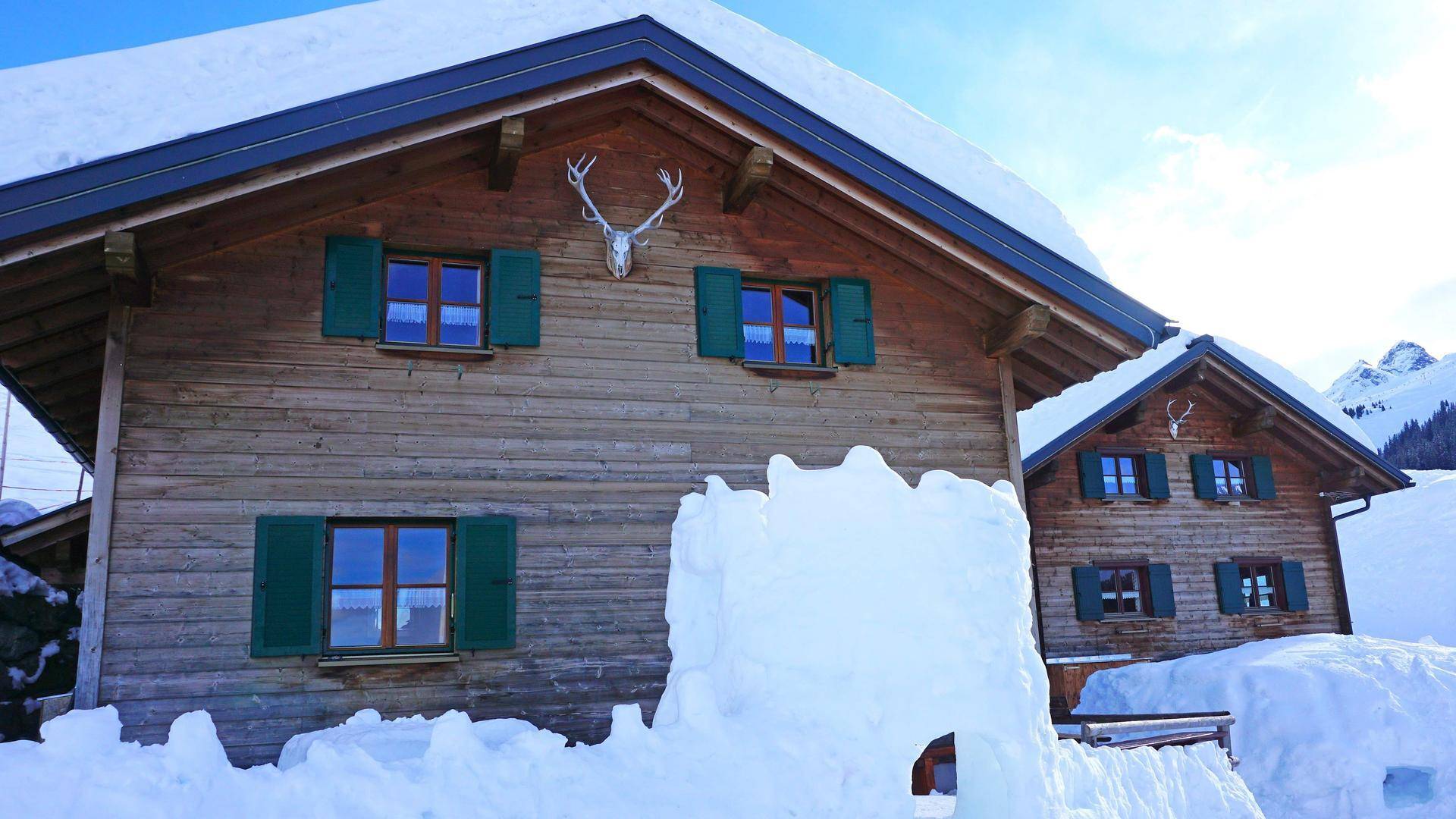 Traditionelles Holzchalet mit grünen Fensterläden, umgeben von Schnee und Bergen.