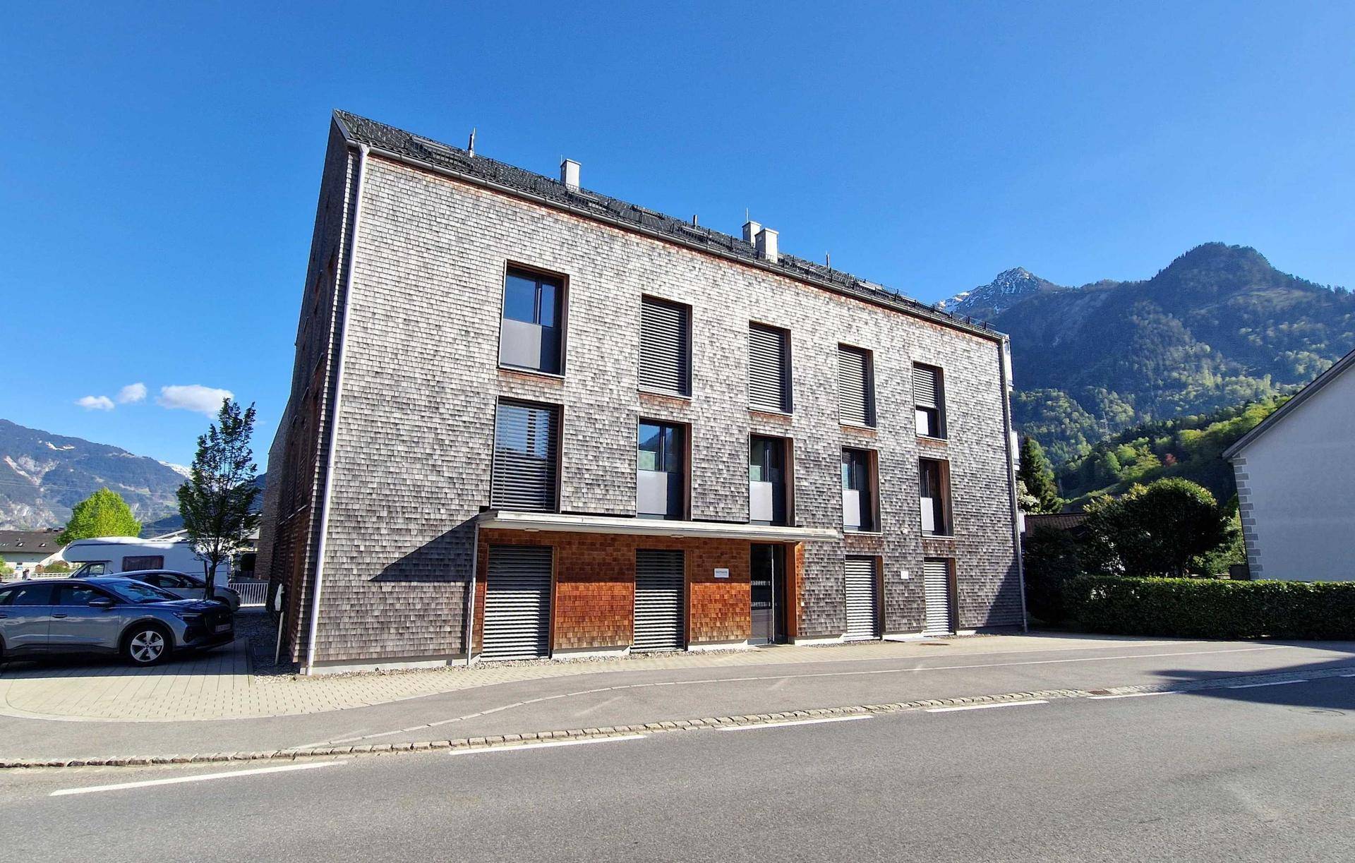 Ansicht eines modernen Gebäudes mit Holzschindelfassade und Fenstern, im Hintergrund Berge.