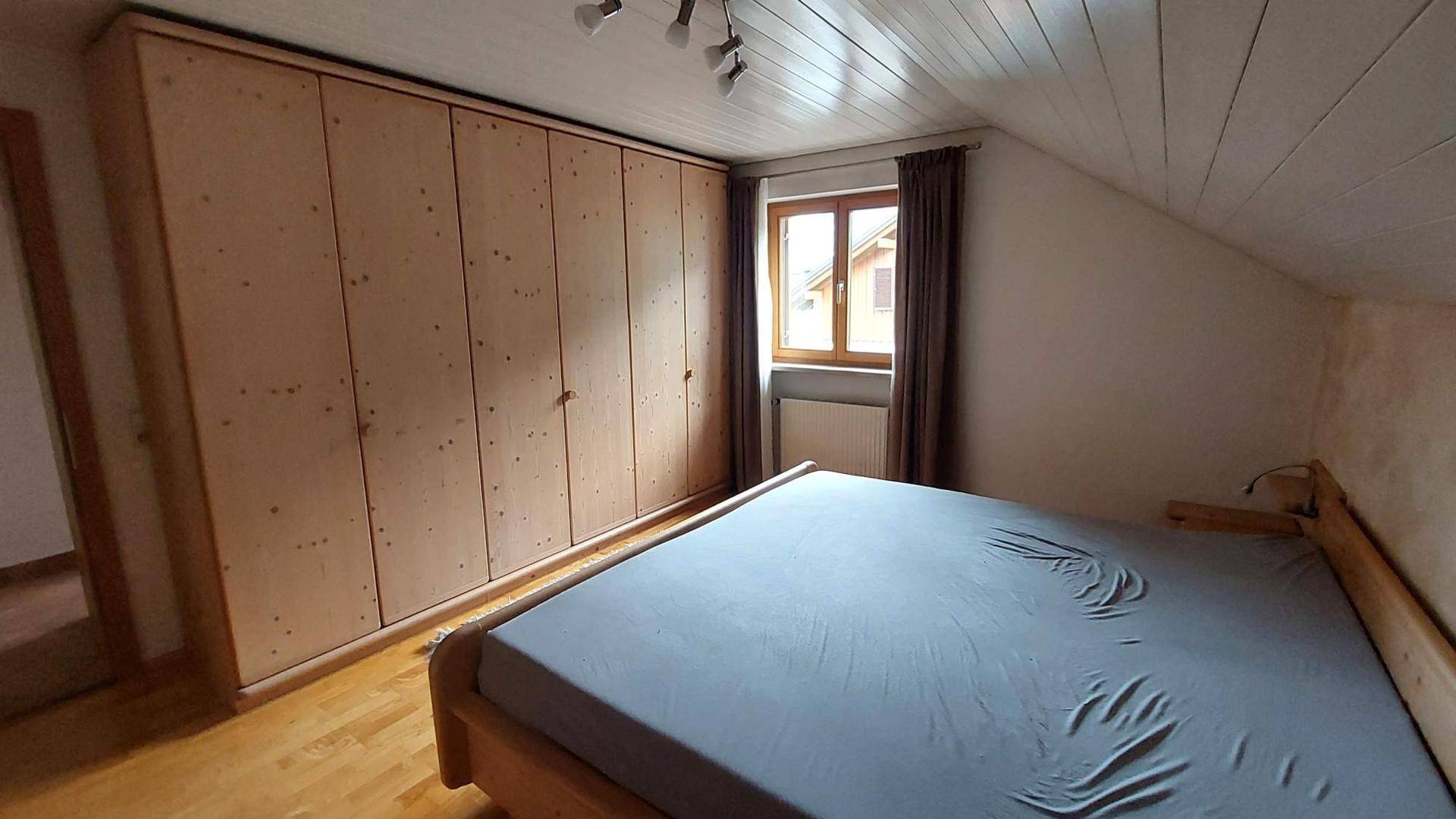 Schlafzimmer im Dachgeschoss mit großem Einbauschrank aus Holz, Holzboden und Fenster.