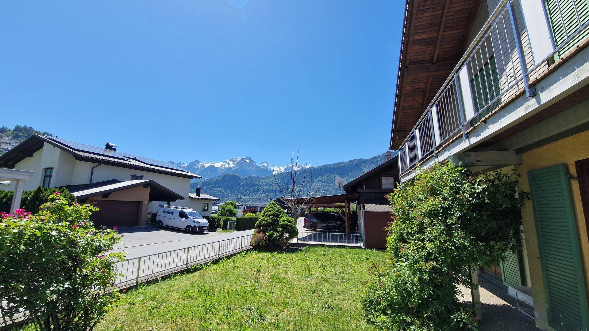 Sonniger Gartenbereich mit Rasen, Carport und beeindruckendem Bergblick in der Ferne.