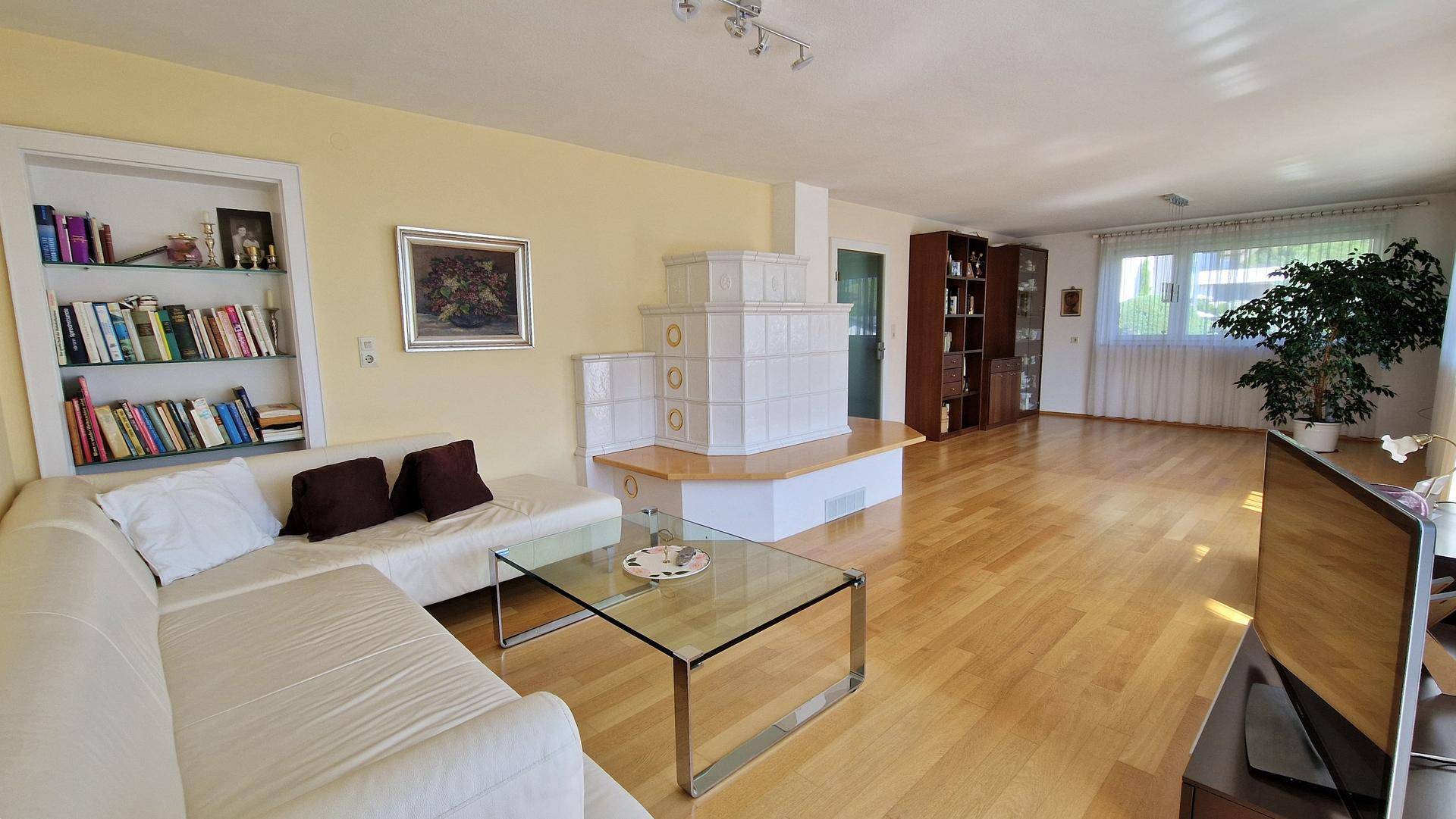 Geräumiges Wohnzimmer mit hellem Parkettboden, Kachelofen und gemütlicher Sitzecke.
