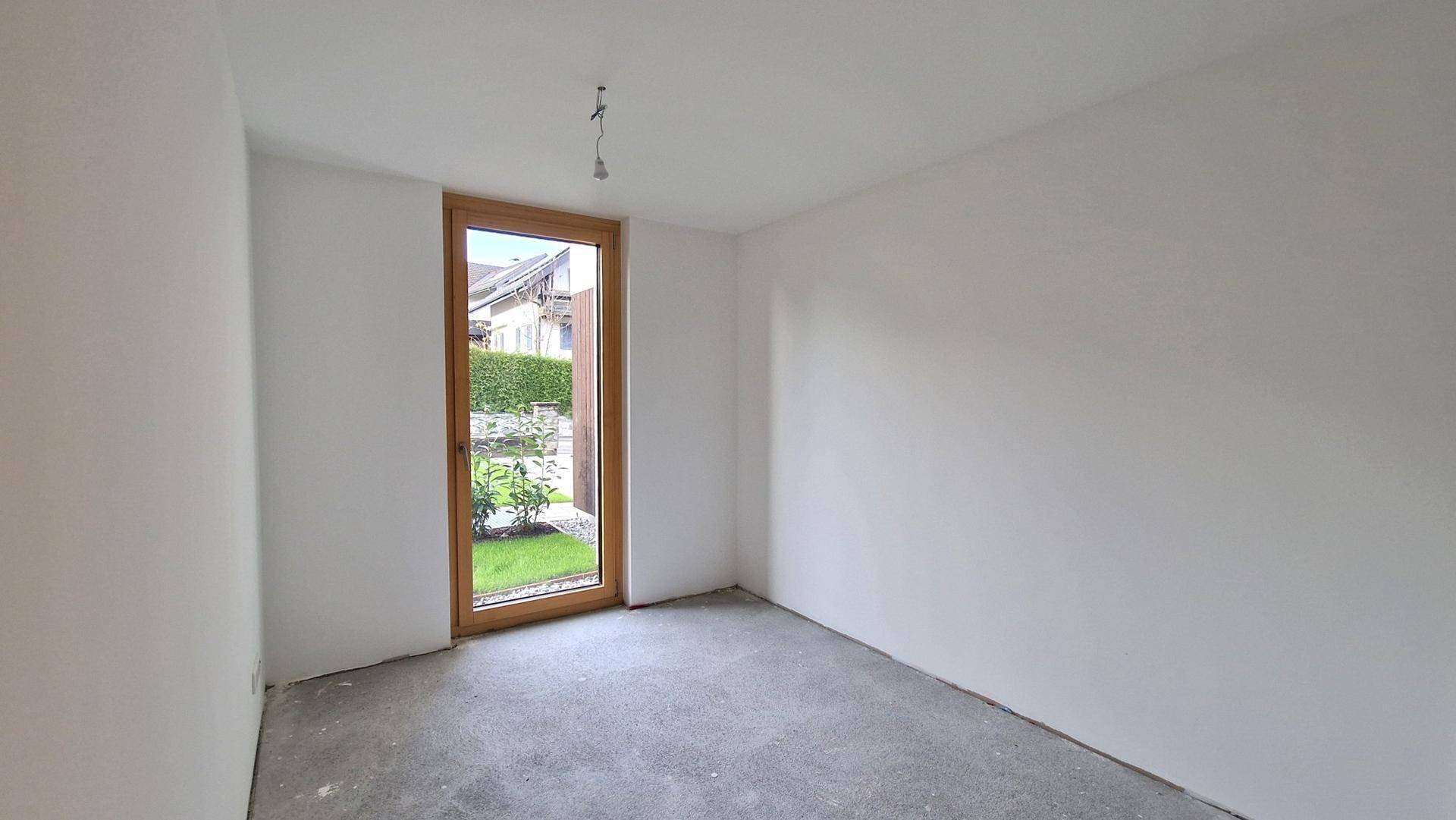 Kleiner, heller Raum im Rohbauzustand mit Fenster zum Garten, wartet auf Fertigstellung.