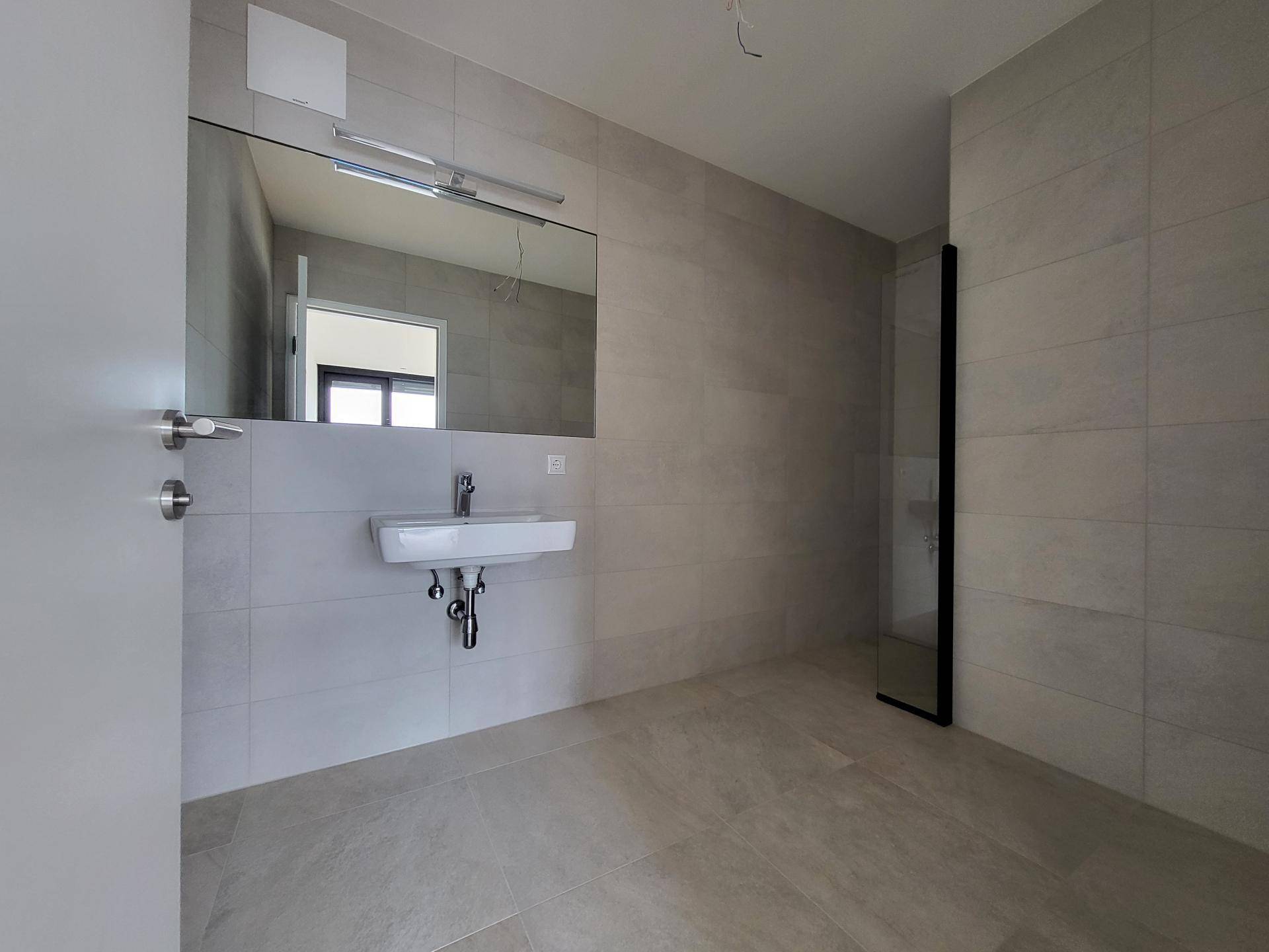 Modernes Badezimmer mit hellen Fliesen, großem Spiegel und begehbarer Dusche.