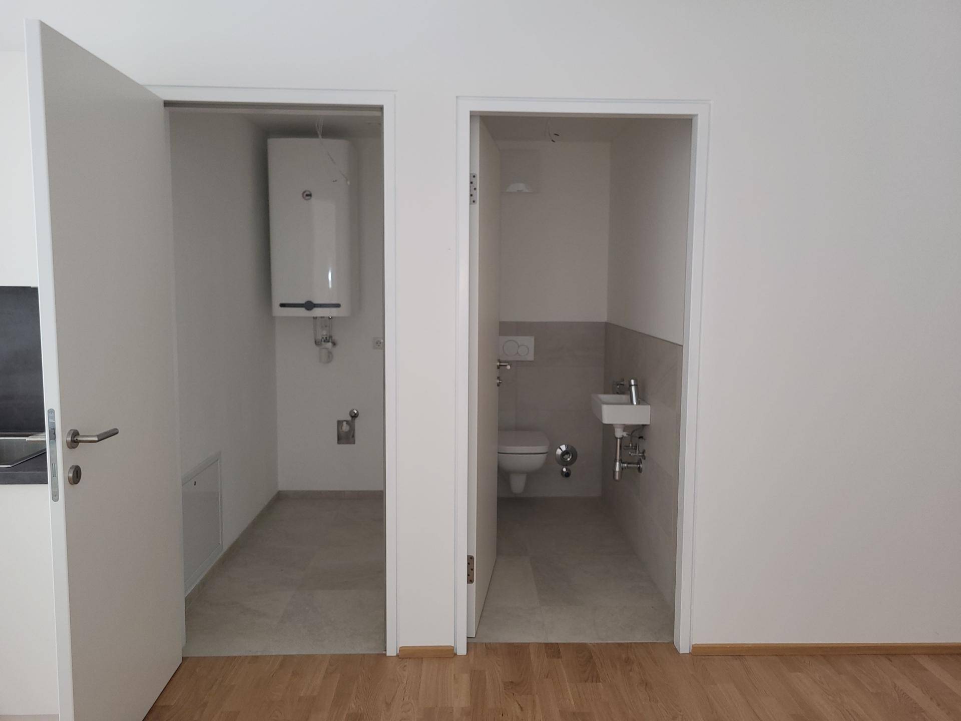 Zwei offene Räume, darunter ein Gäste-WC und ein Hauswirtschaftsraum mit Warmwasserboiler.