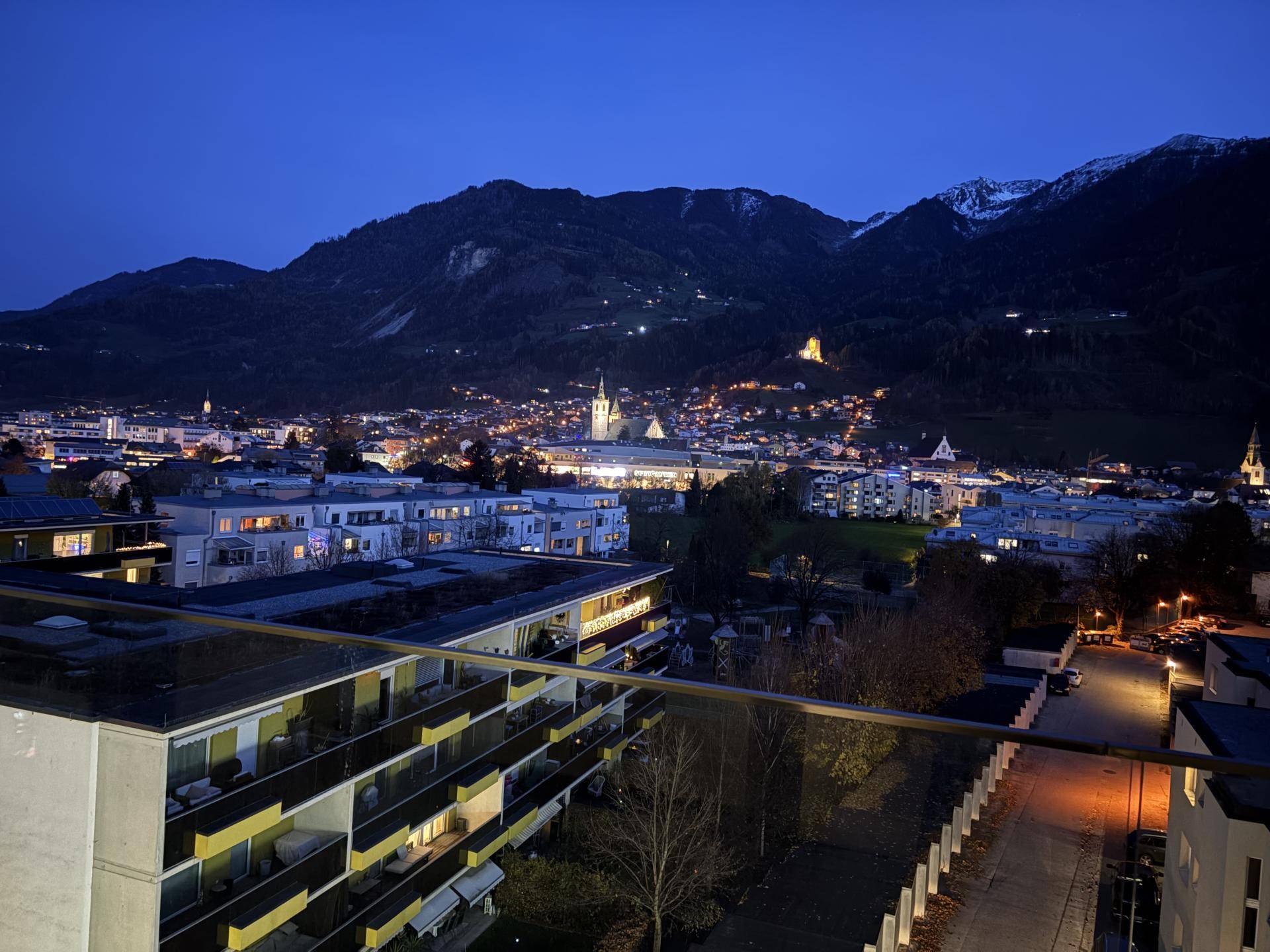 Nächtlicher Ausblick auf die beleuchtete Stadt und die dunklen Berge im Hintergrund.
