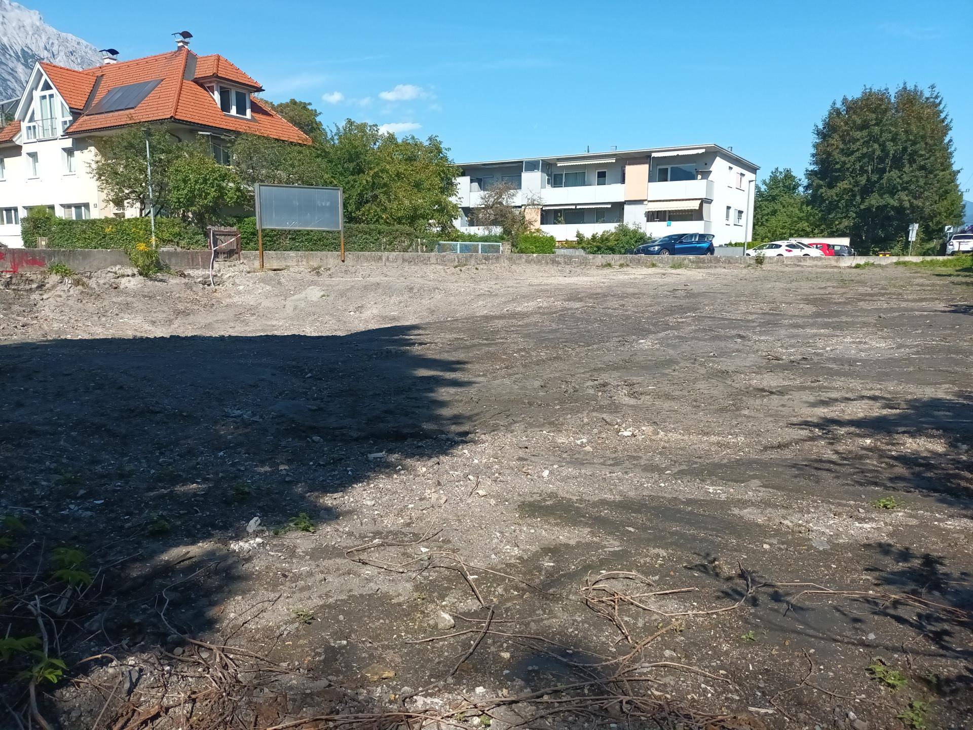 Freies Baugrundstück mit Blick auf umliegende Gebäude und Berge im Hintergrund.