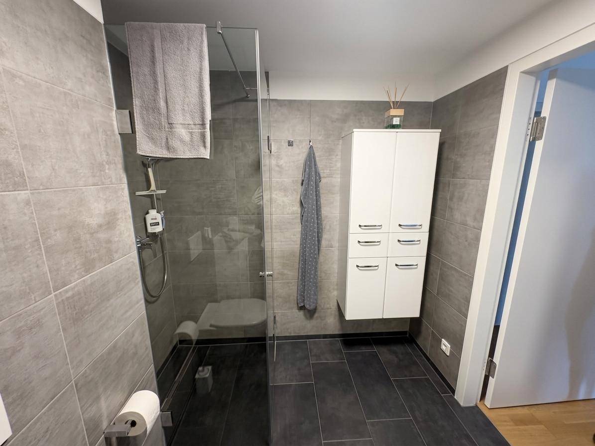 Zeitgemäßes Badezimmer mit großer begehbarer Dusche und eleganten grauen Fliesen.