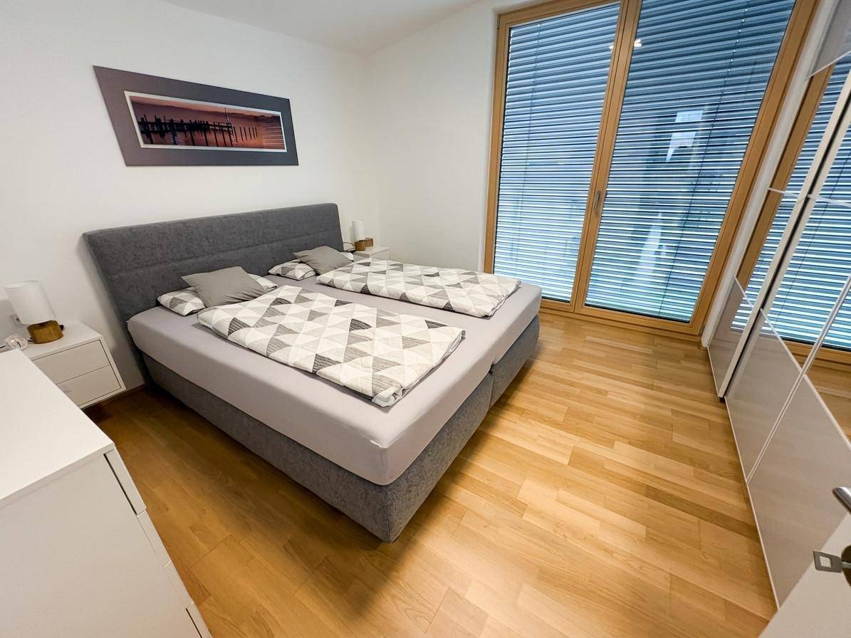Helles Schlafzimmer mit Doppelbett, Holzboden und großen Fenstern für viel Tageslicht.