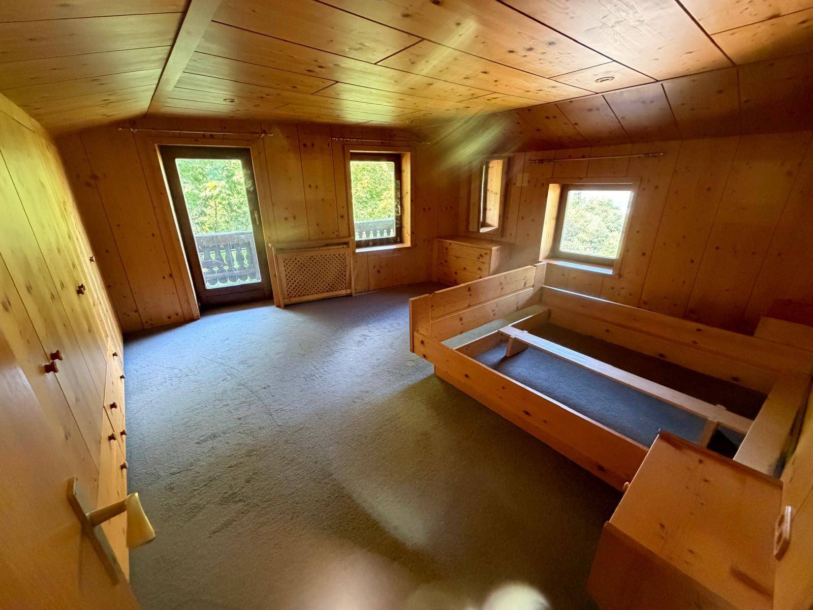 Schlafzimmer im alpinen Stil mit Holzvertäfelung, Teppichboden und Zugang zum Balkon.