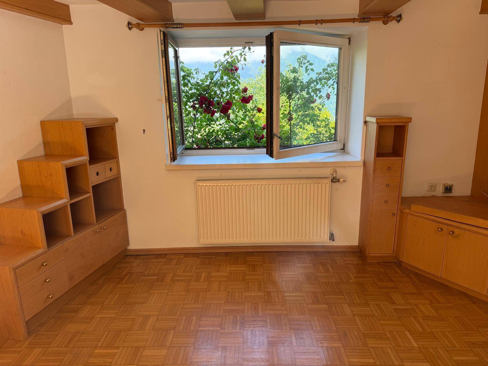 Heller Raum mit Holzparkettboden, Holzmöbeln und einem Fenster mit Bergblick.