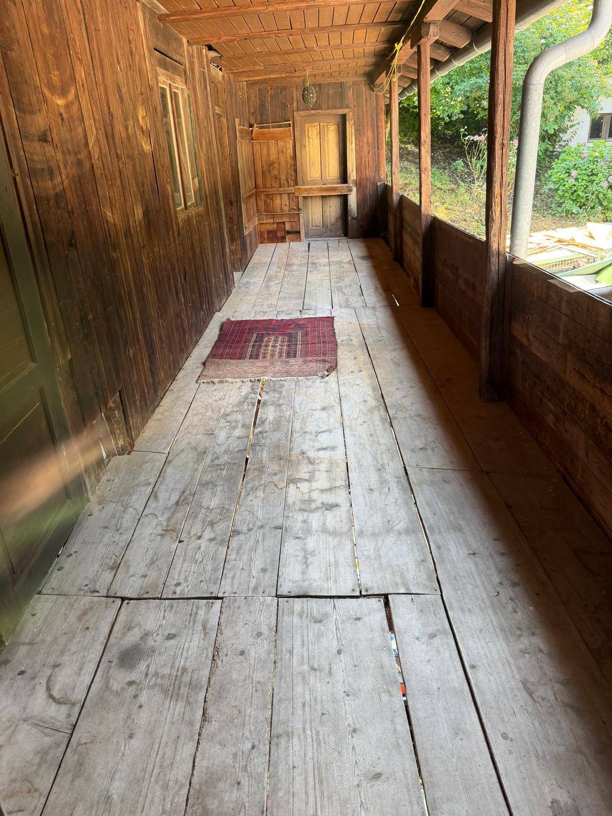 Langer, überdachter Holzbalkon mit Dielenboden und rustikaler Holzverkleidung.