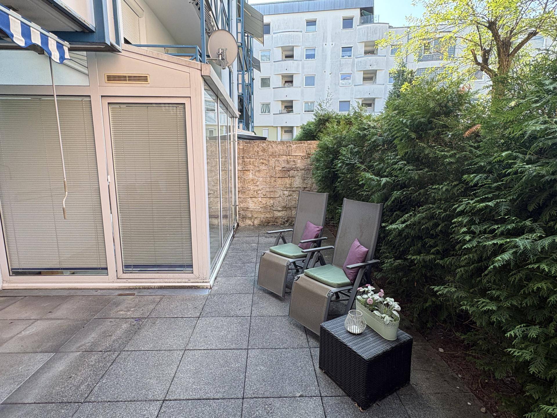 Gartenbereich mit Liegestühlen und Blick auf den Wintergarten sowie die umliegenden Gebäude.