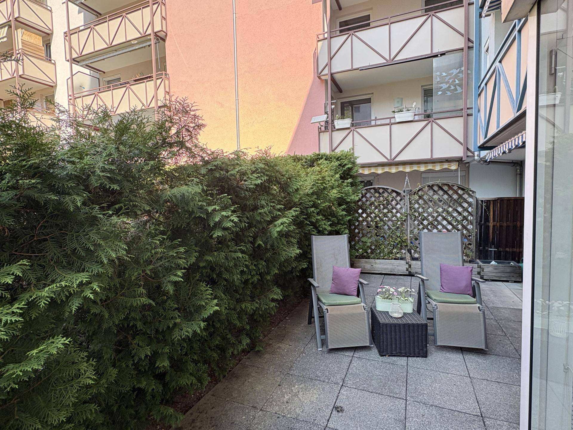 Gartenbereich mit Liegestühlen und einem Beistelltisch, umgeben von einer Hecke und Holzelementen.