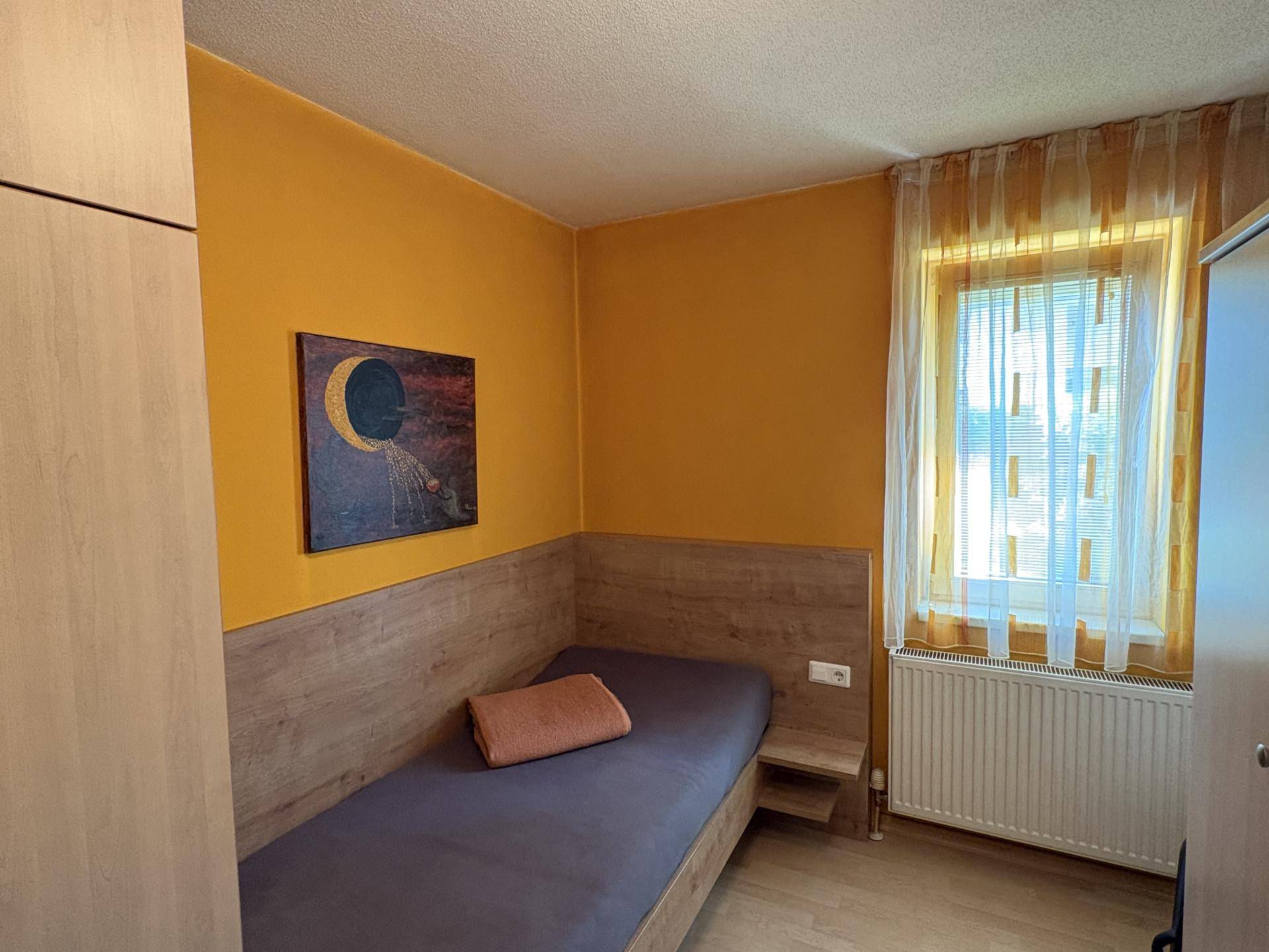 Gemütliches Schlafzimmer mit Einzelbett, Holzvertäfelung und gelben Wänden, ideal als Gästezimmer.
