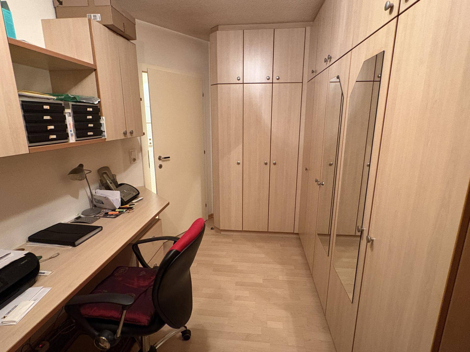 Funktionales Arbeitszimmer mit Schreibtisch, Bürostuhl und vielen Einbauschränken für Stauraum.