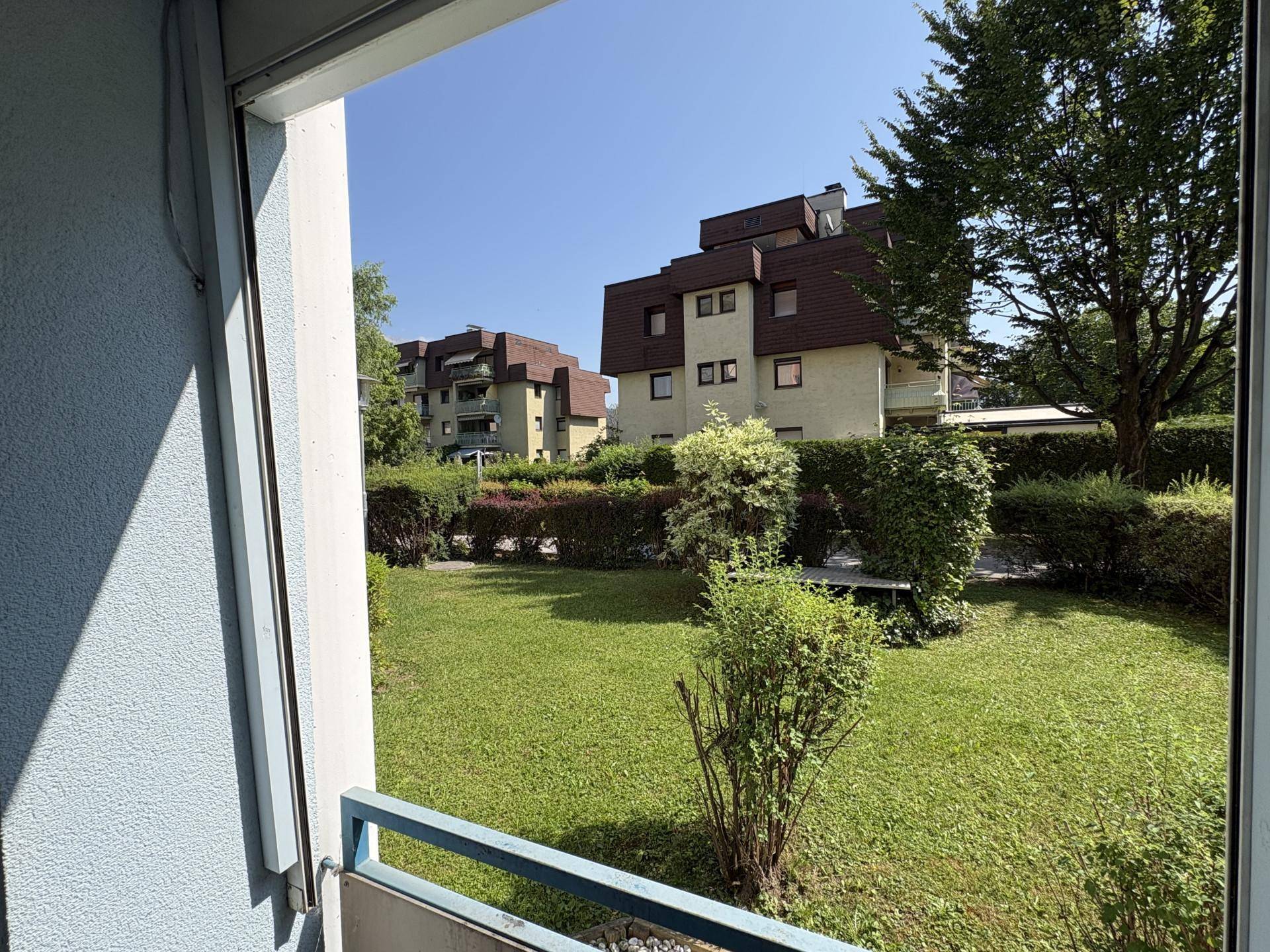 Blick von einem Balkon auf eine grüne Gartenanlage und weitere Wohngebäude.
