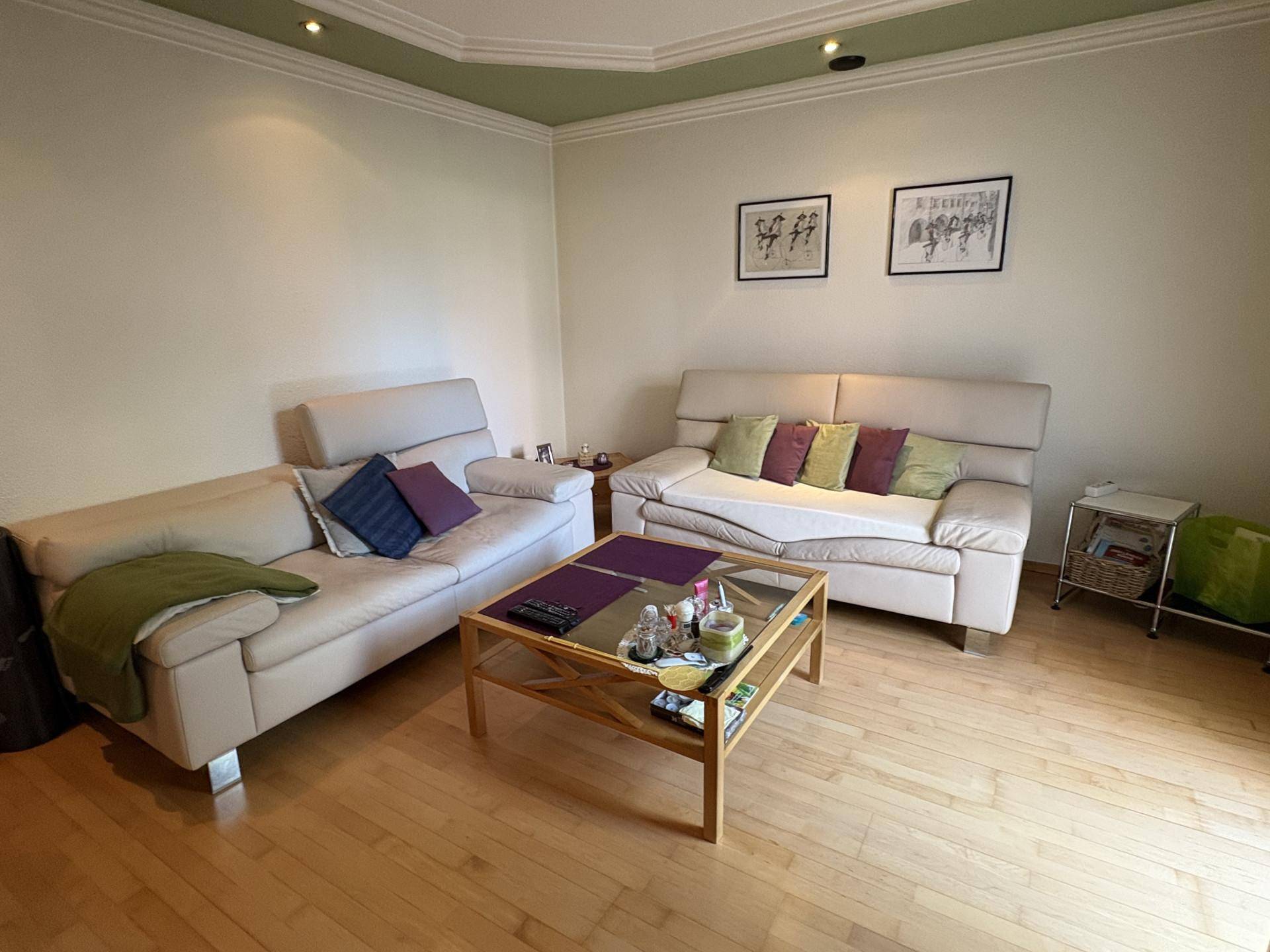 Geräumiges Wohnzimmer mit zwei hellen Sofas, Couchtisch und Parkettboden, ideal zum Entspannen.