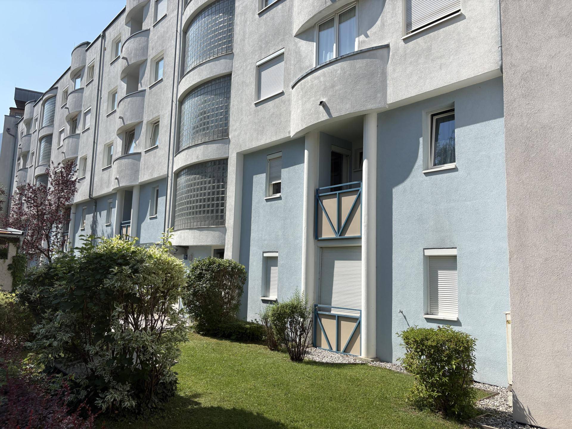 Moderne Gebäudefassade mit großen Fenstern, Glasbausteinen und gepflegter Grünanlage.