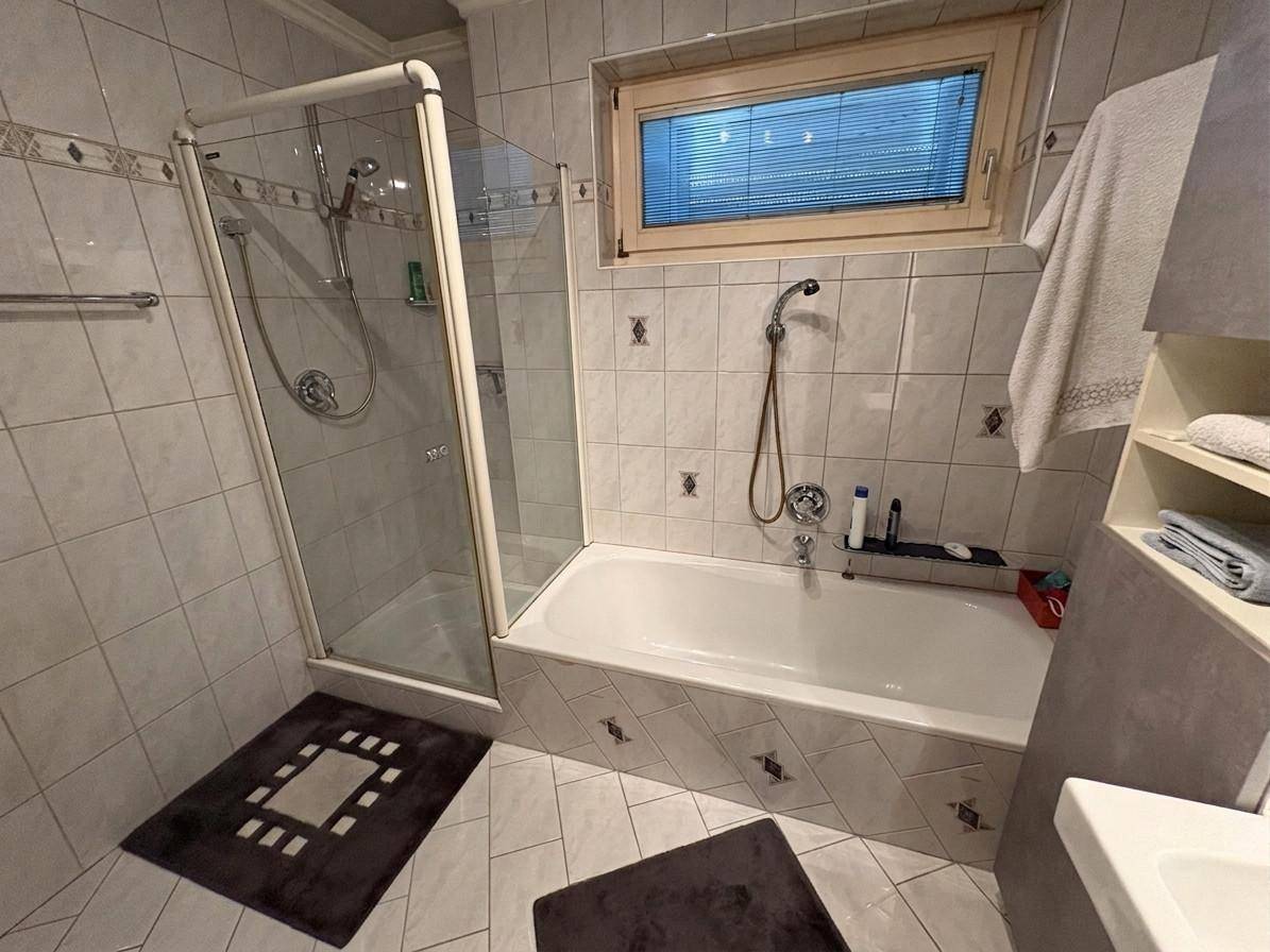 Badezimmer mit Badewanne, Duschkabine und Fenster, ausgestattet mit hellen Fliesen.