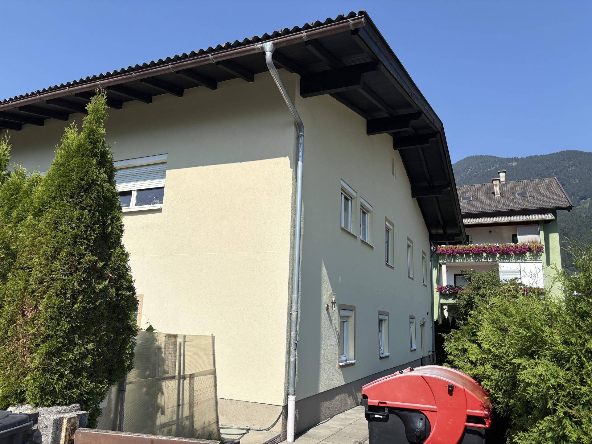 Seitenansicht des Hauses mit Dachrinne und grüner Bepflanzung im Vordergrund.