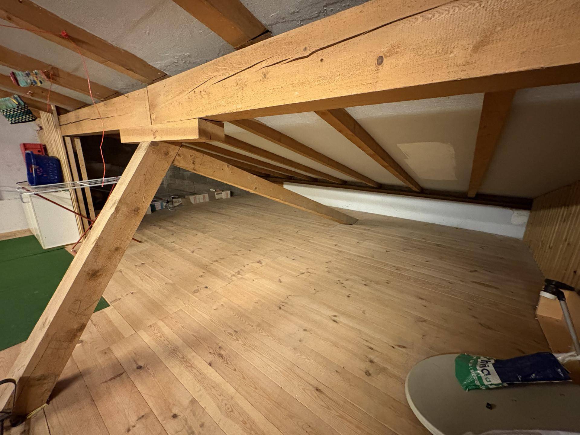 Dachbodenraum mit sichtbaren Holzbalken und Holzdielenboden, als Abstellfläche genutzt.
