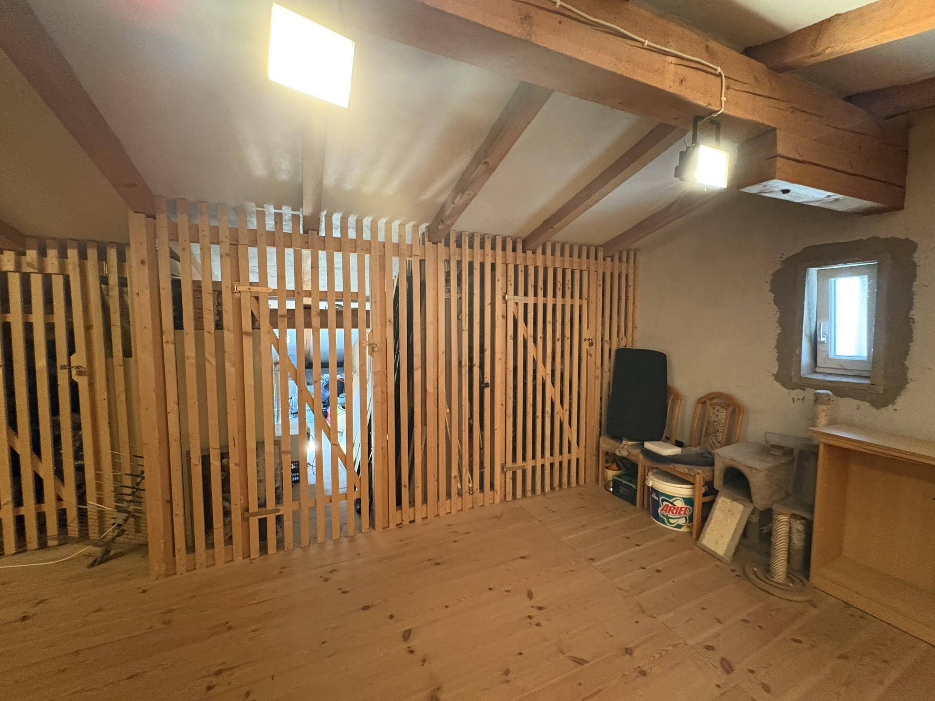 Geräumiger Dachboden mit Holzlattenwänden und kleinem Fenster, ideal für Lagerung.