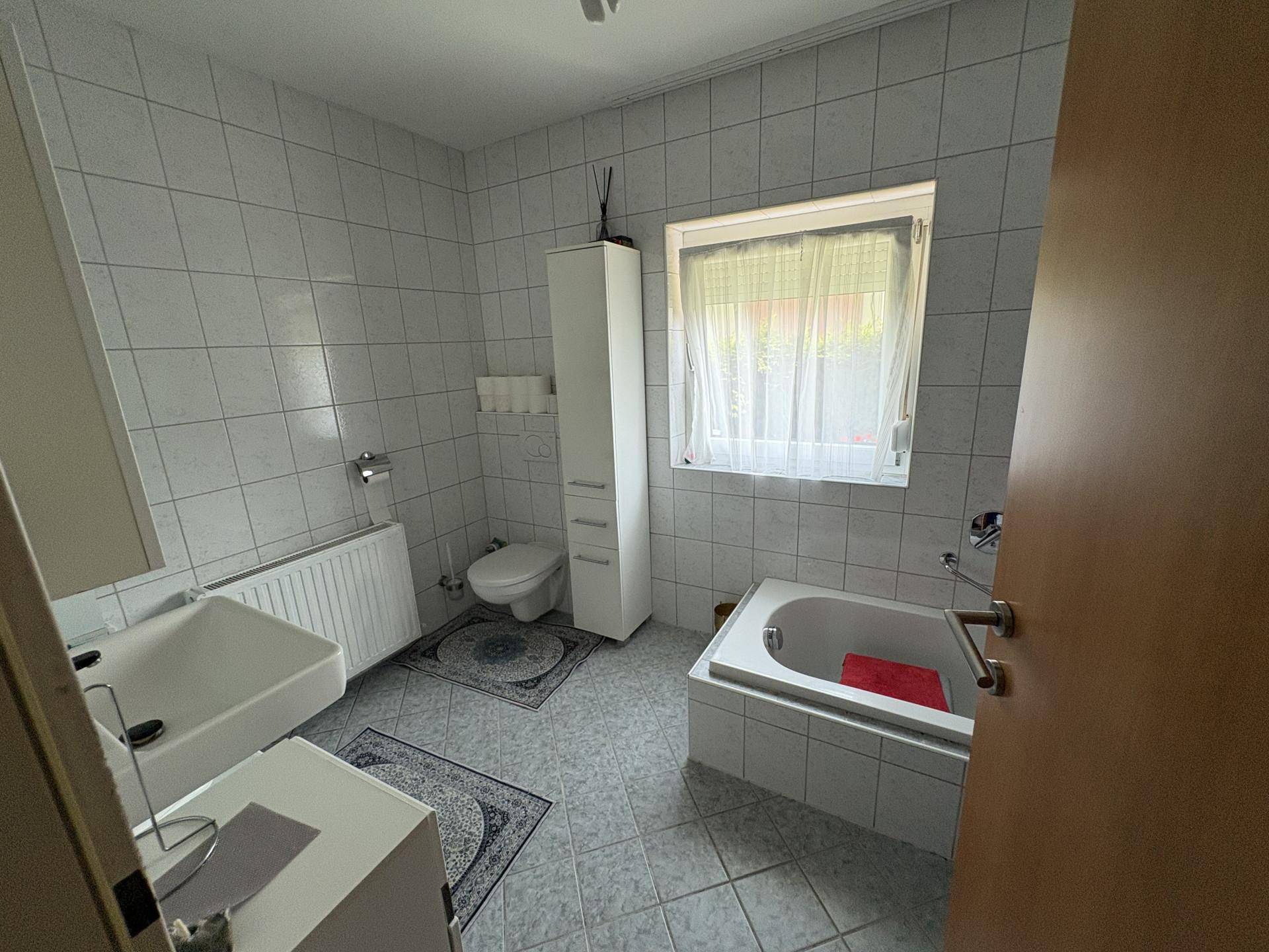 Badezimmer mit hellblauen Fliesen, Badewanne, WC und Fenster für Tageslicht.