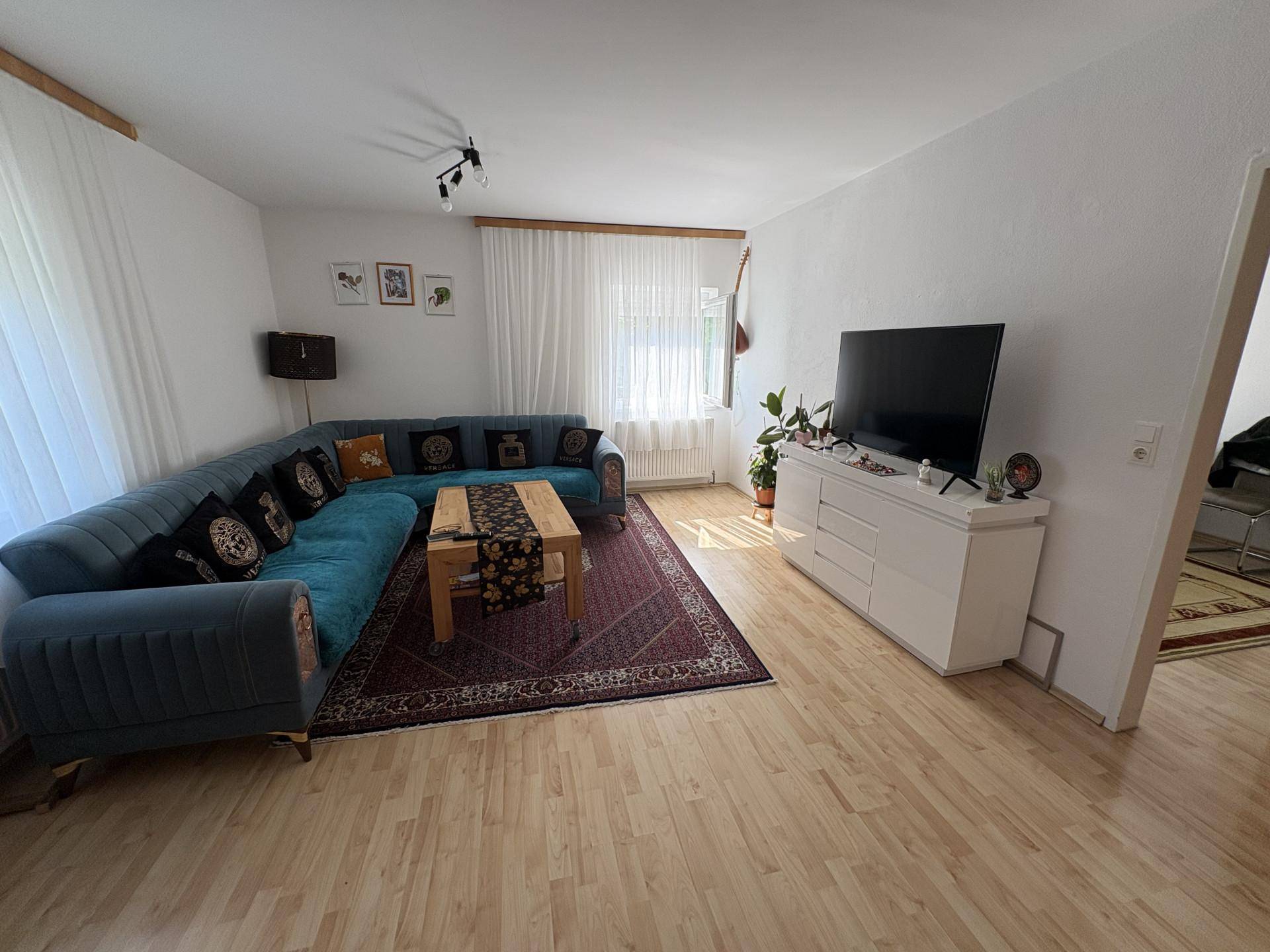 Gemütliches Wohnzimmer mit großem Ecksofa, Holzboden und viel Tageslicht.
