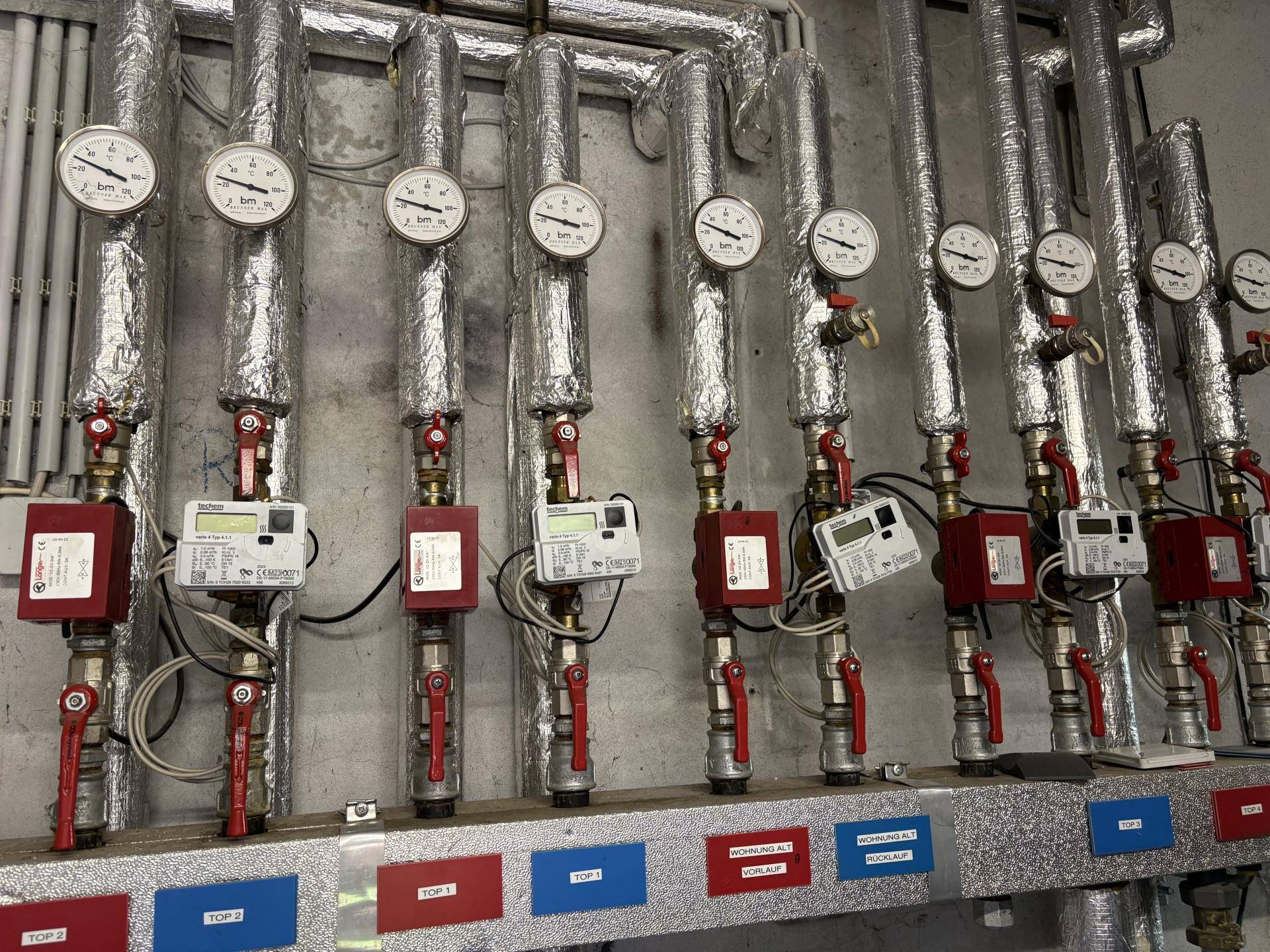 Heizungsanlage mit isolierten Rohren, Manometern und Wärmezählern.