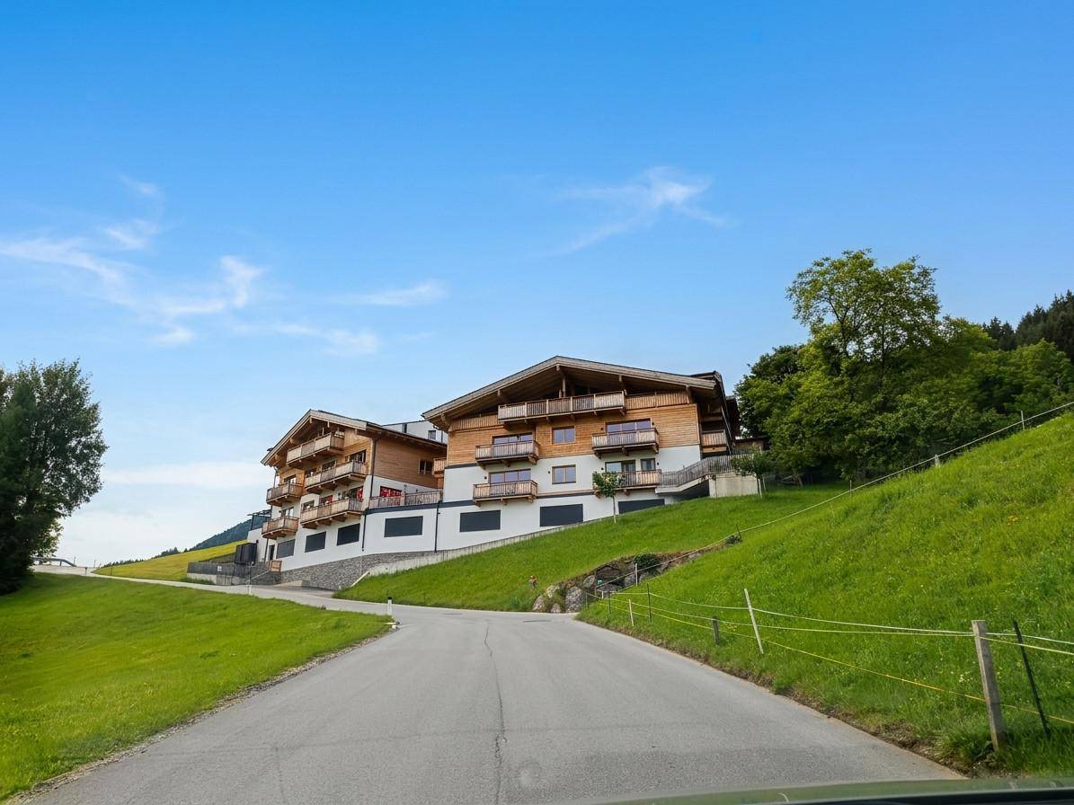 Attraktives Mehrfamilienhaus in alpiner Architektur, eingebettet in grüne Hügellandschaft.
