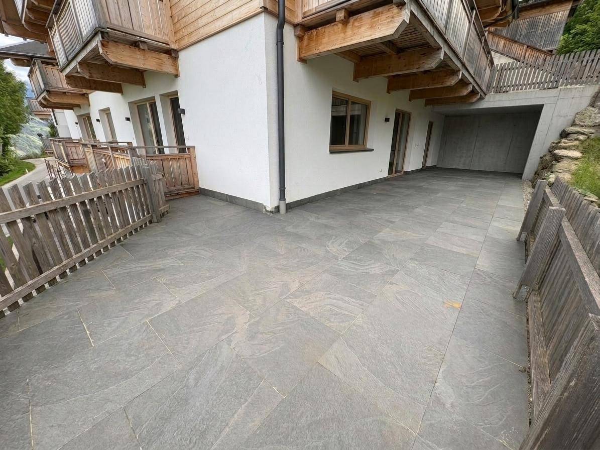 Geräumige Außenterrasse mit grauen Fliesen und traditionellen Holzbalkonen am Gebäude.