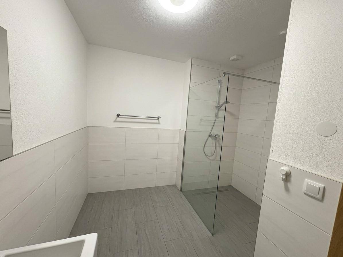 Modernes Badezimmer mit begehbarer Dusche, hellen Fliesen und minimalistischem Design.