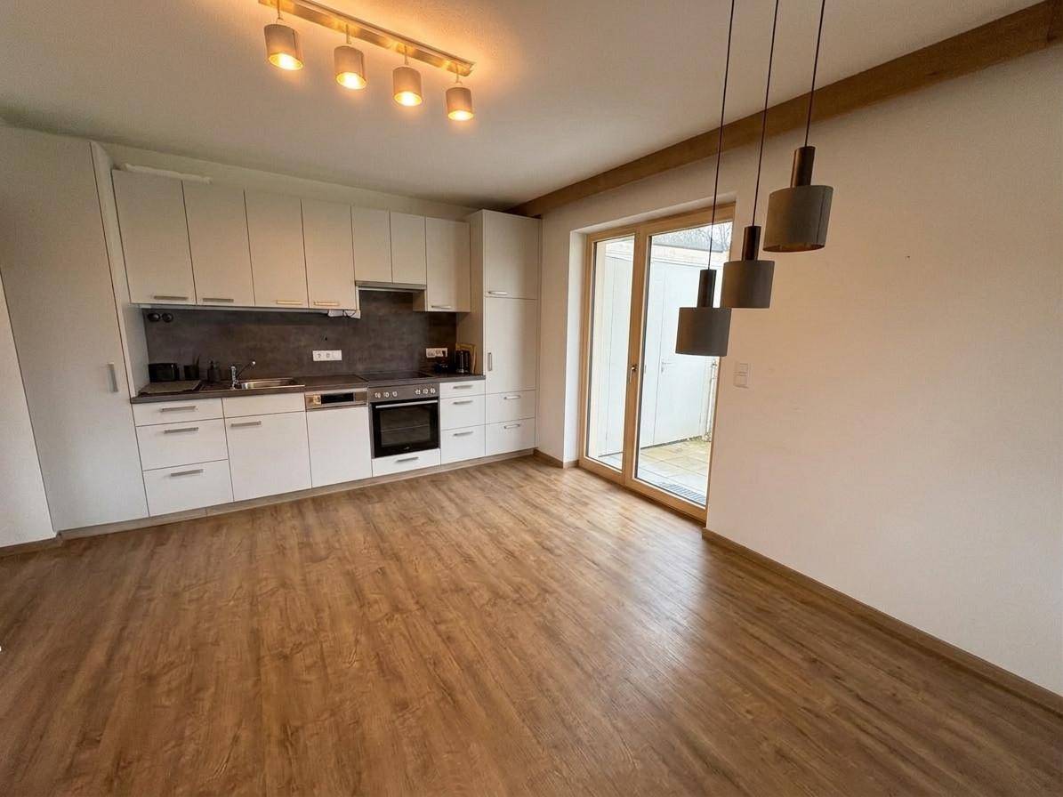 Moderne Einbauküche mit weißen Schränken, integriertem Backofen und Zugang zur Terrasse.