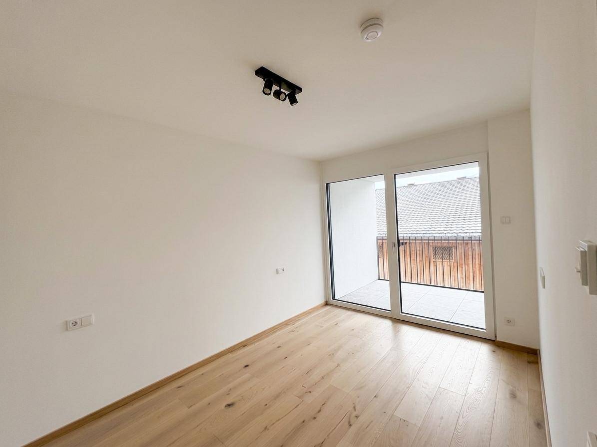 Helles Zimmer mit Holzboden und großzügigem Zugang zu einem Balkon oder einer Terrasse.