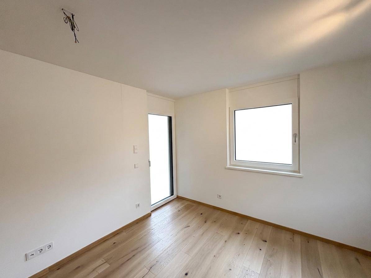 Leeres Zimmer mit hellem Holzfußboden und Zugang zu einem französischen Balkon.