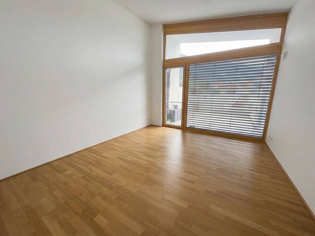 Helles Zimmer mit Holzboden und großen Fenstern, ideal als Wohn- oder Schlafbereich.