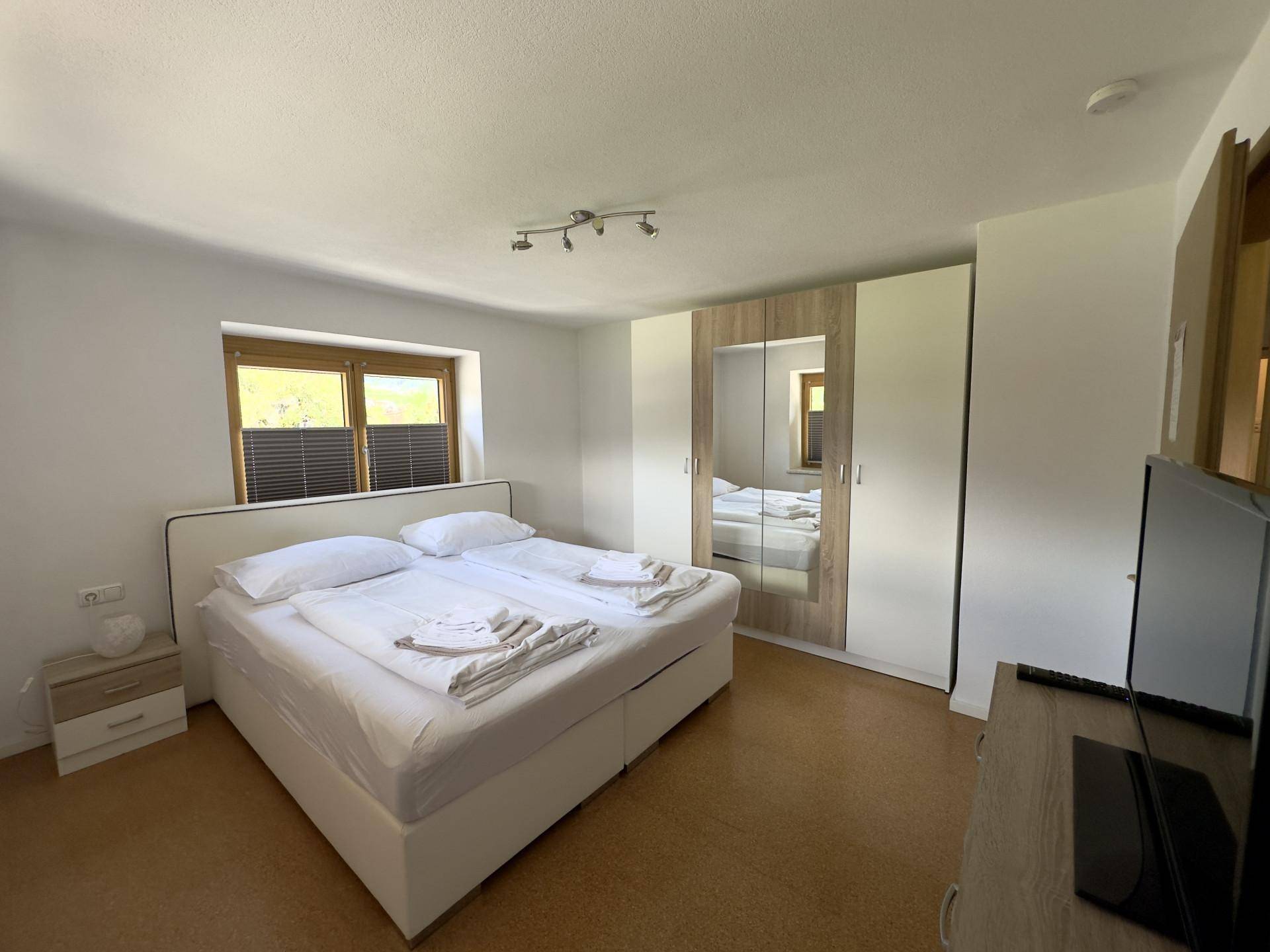Schlafzimmer mit Doppelbett, großem Spiegelschrank und Fenster für angenehmes Tageslicht.