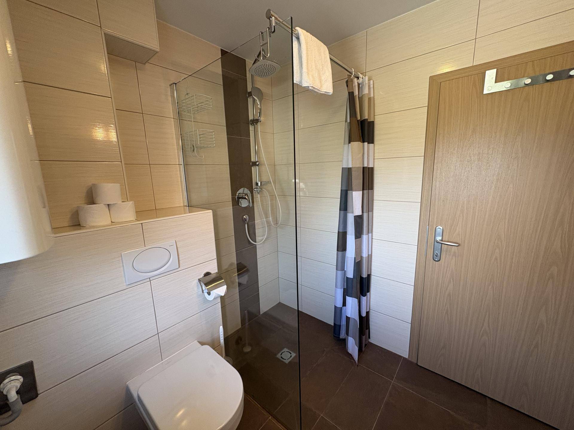 Badezimmer mit ebenerdiger Dusche, wandhängendem WC und modernen Fliesen in Beige- und Brauntönen.