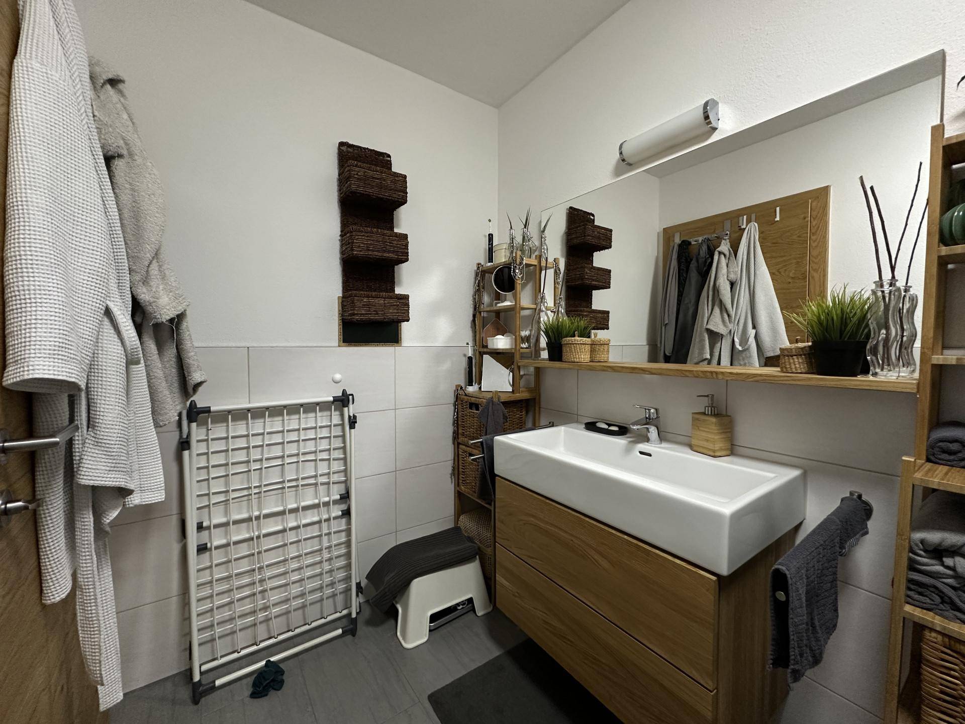 Modernes Badezimmer mit einem stilvollen Holzwaschtisch, großem Spiegel und praktischen Ablagemöglichkeiten.